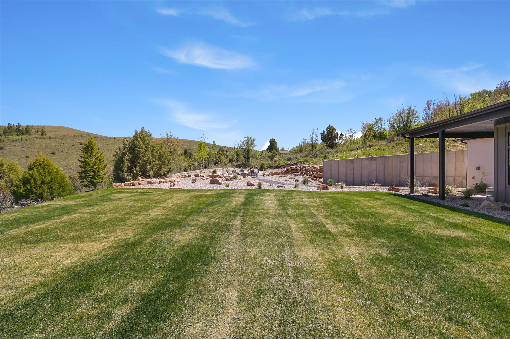 Expansive rear lawn with a retaining wall, a covered patio, and a xeriscaped area featuring rock details