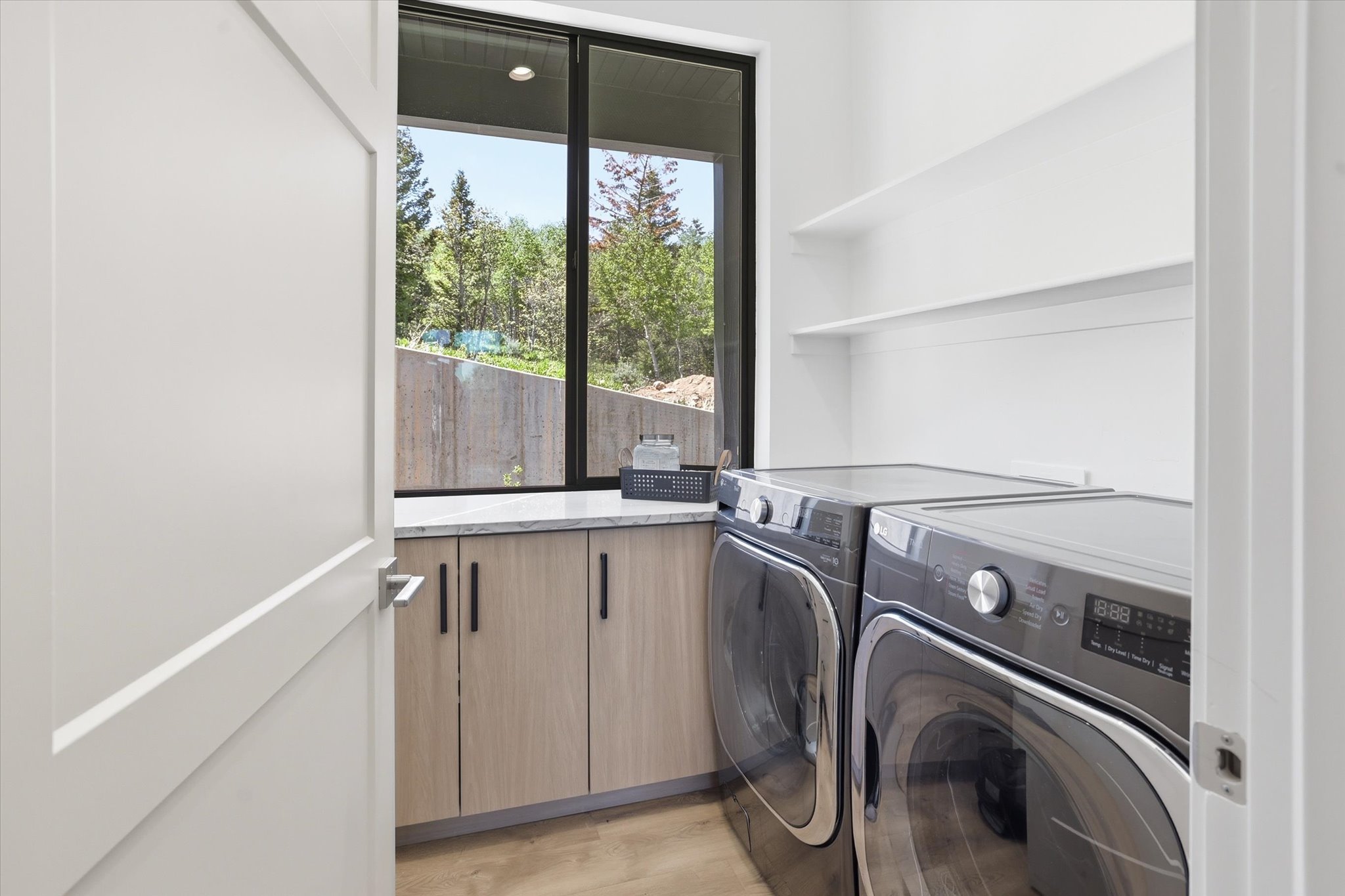 Laundry area featuring stacked appliances, light wood-finish cabinetry, a stone-finish countertop, and integrated shelving