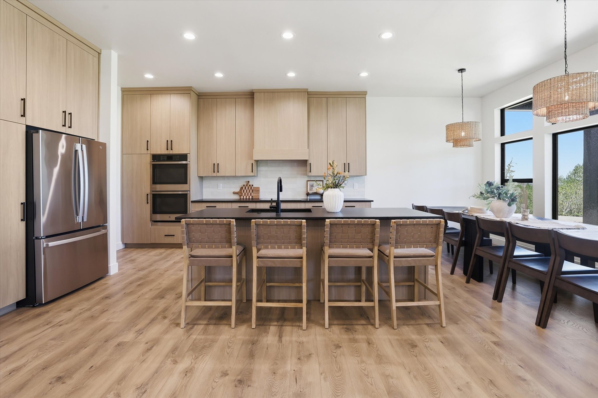 Open-concept kitchen and dining area featuring light wood-finish cabinetry, stainless steel appliances, dark countertops, and wood-finish flooring