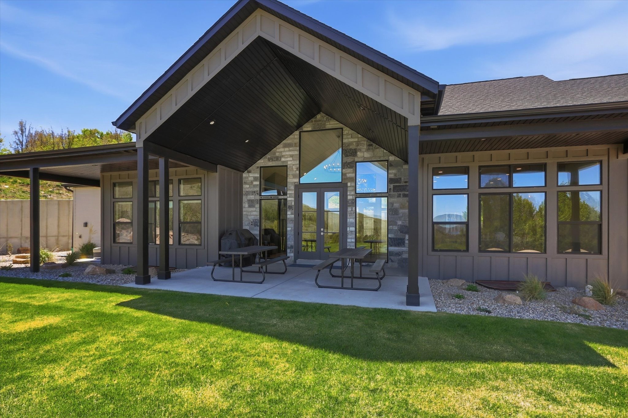 Rear exterior featuring a covered patio with concrete flooring, stone accent wall, and expansive windows
