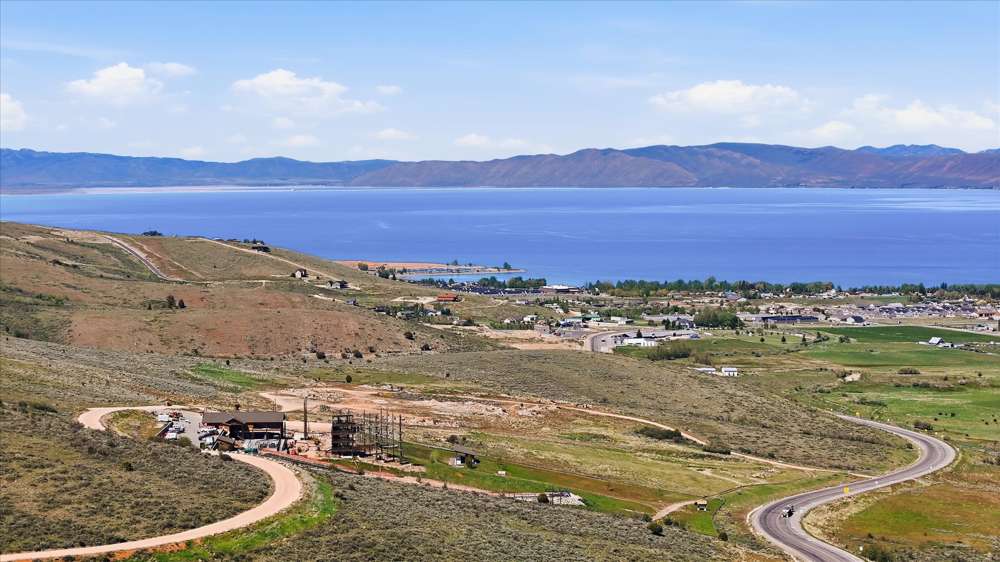 Expansive lakefront property featuring a serene body of water, distant mountain ranges, and an undulating landscape