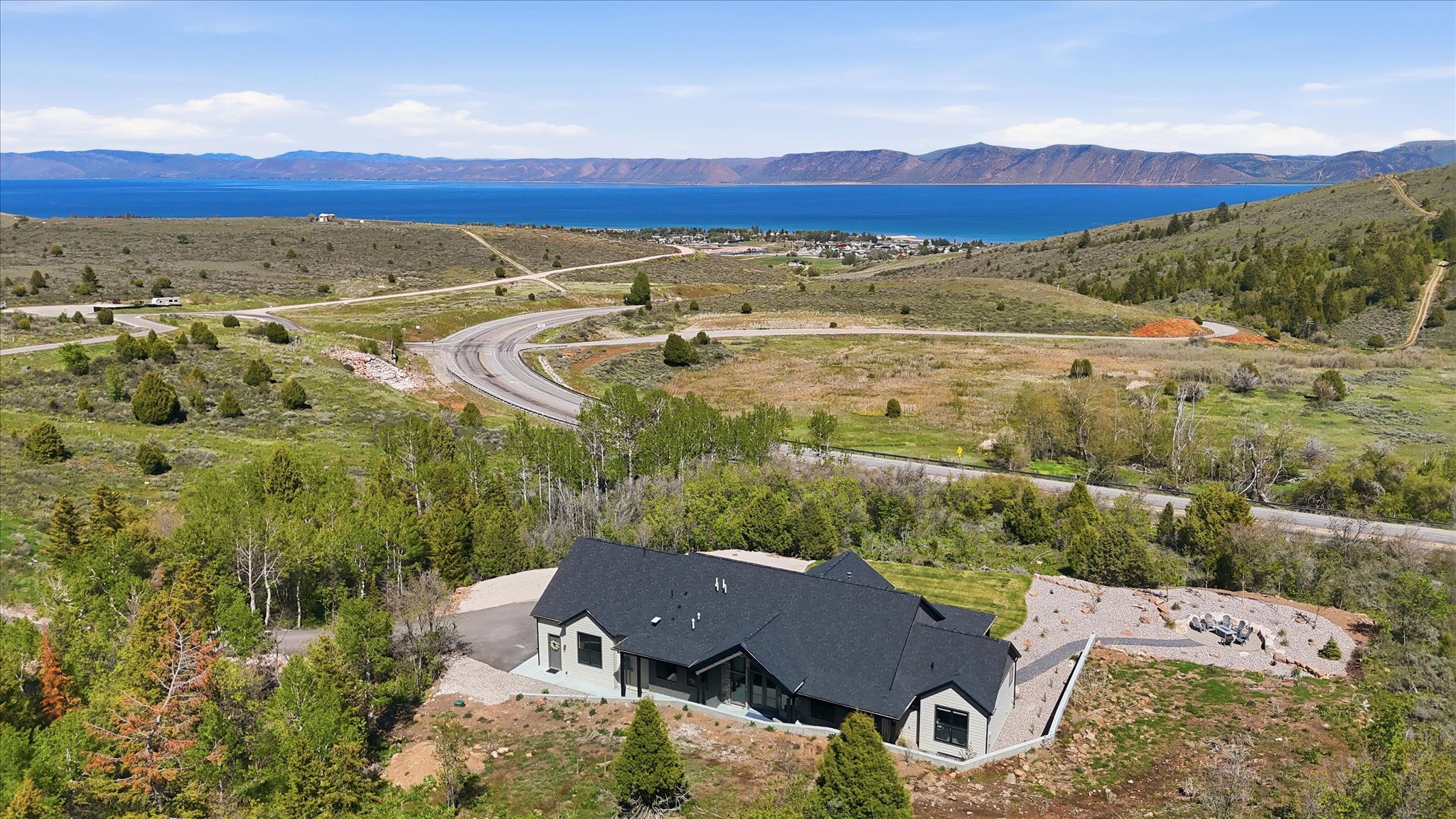 Modern-style home situated on a hillside, featuring a dark shingle roof and light-colored siding
