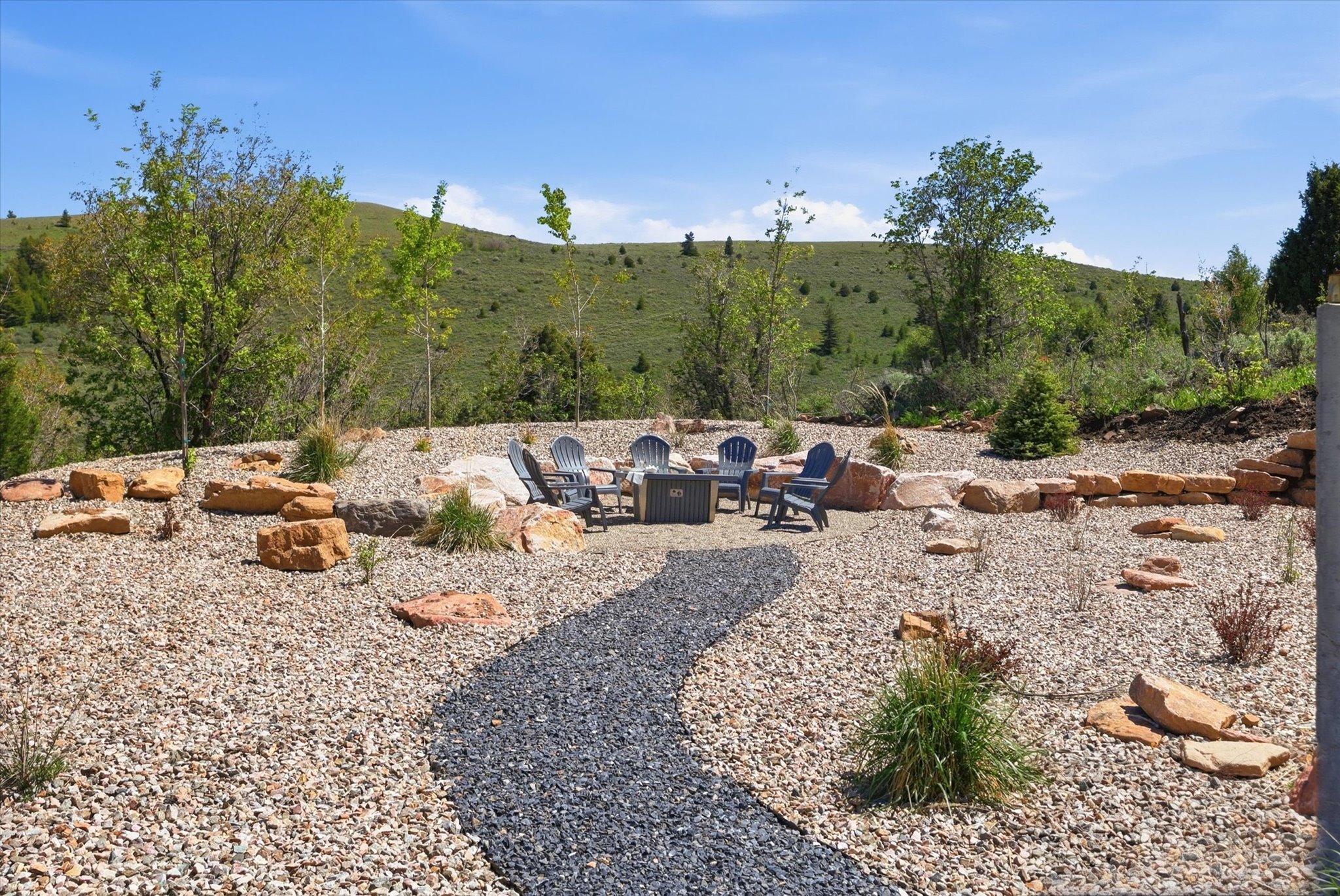 Landscaped outdoor area featuring a central fire pit surrounded by Adirondack chairs