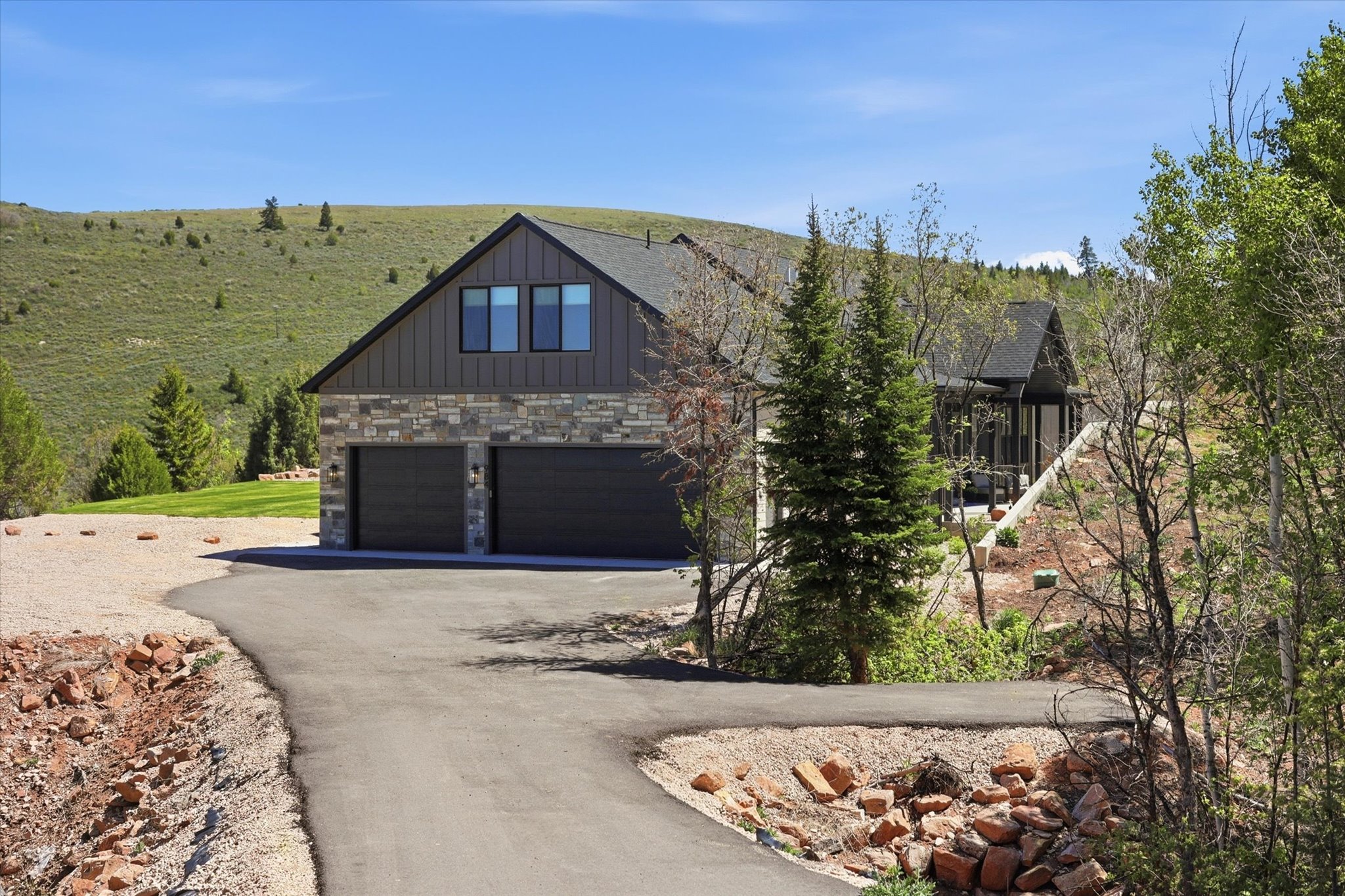 Contemporary residence featuring a two-car garage, stone and vertical siding facade, and multiple windows