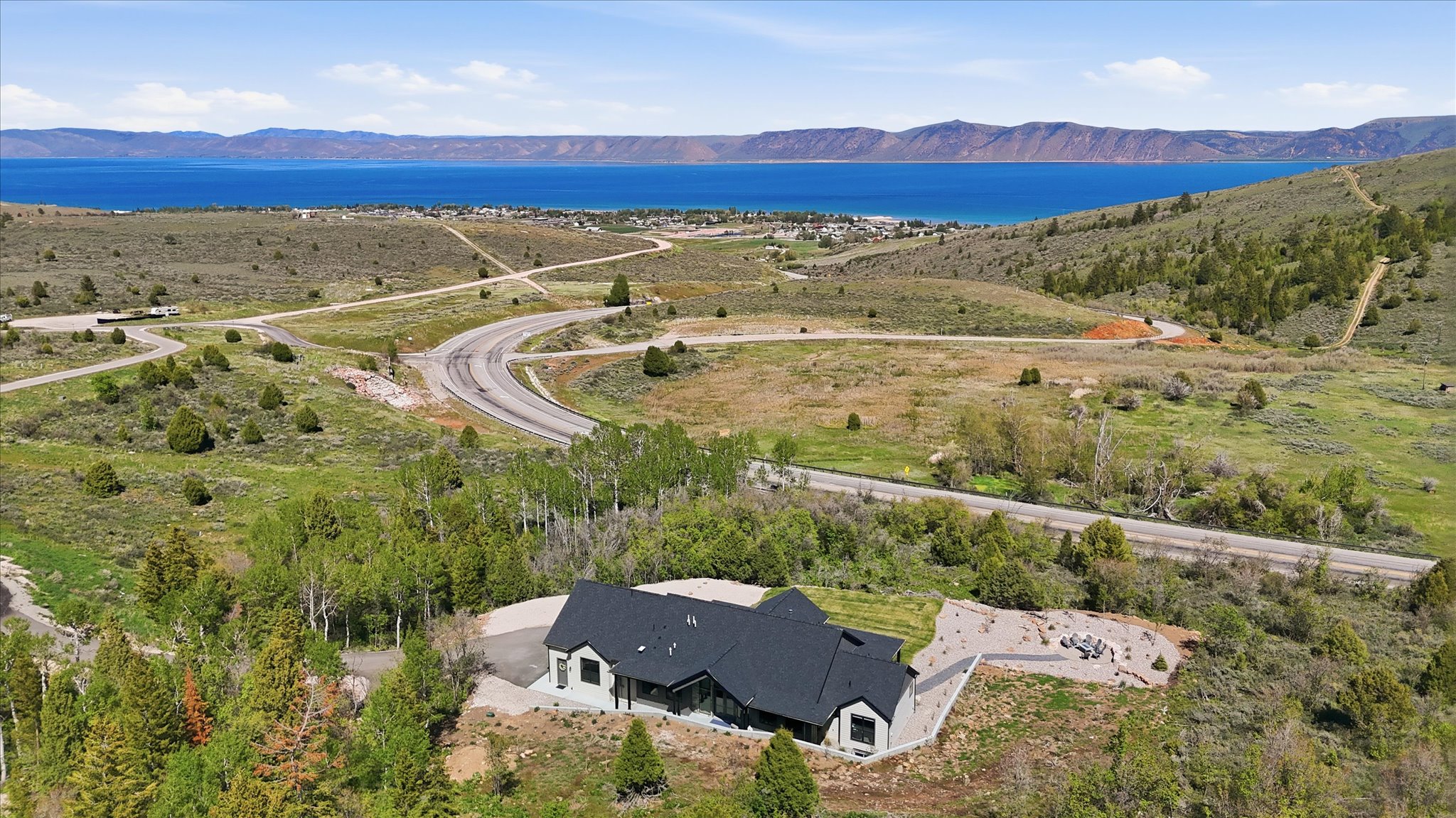 Modern exterior with a dark-pitched roof, light-colored siding, and extensive natural landscaping