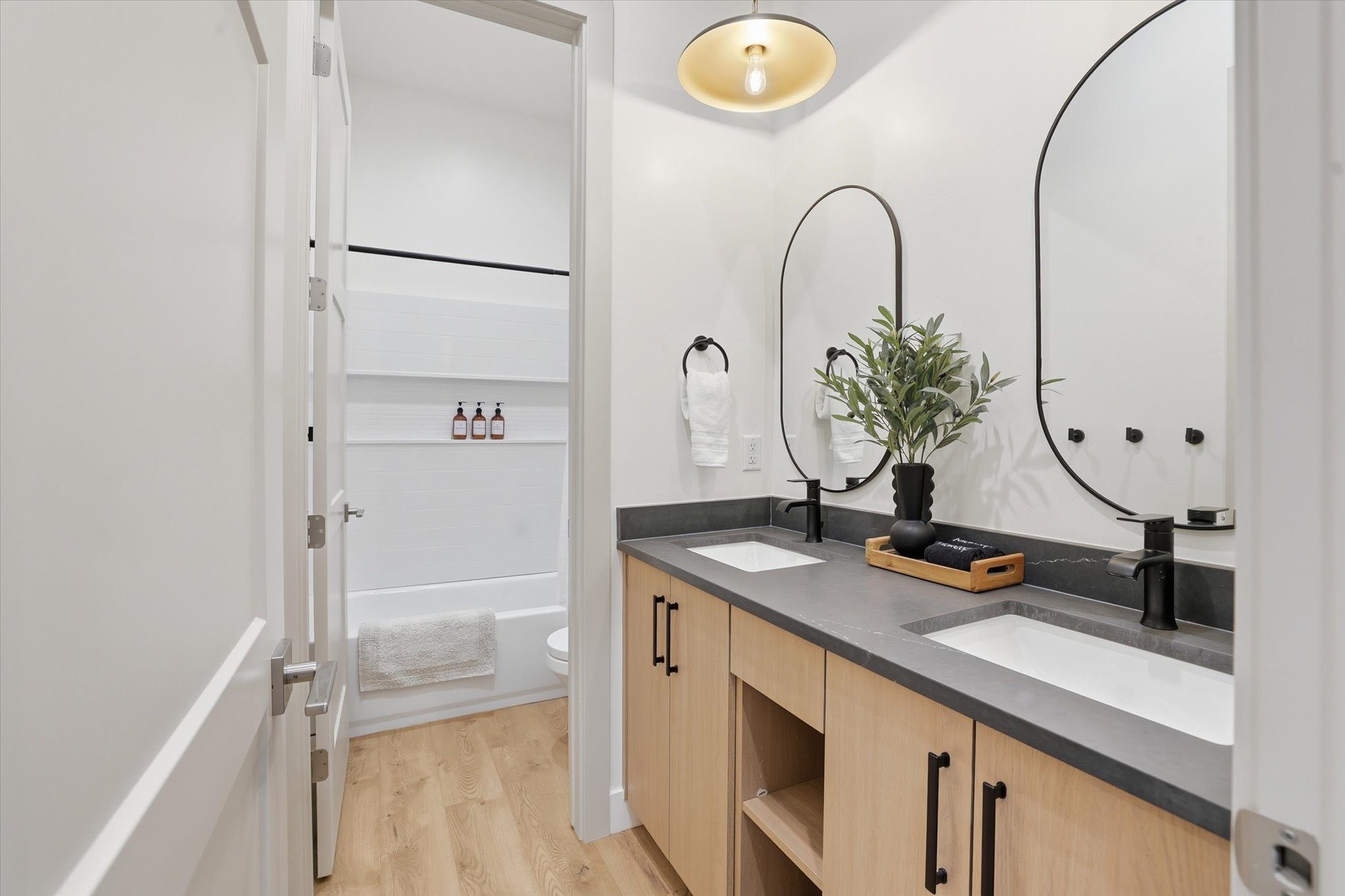 Bathroom featuring a dual vanity with light wood-finish cabinetry, dark countertops, and undermount sinks