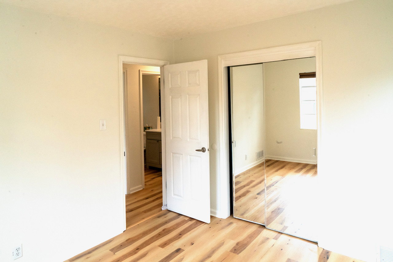 Light wood-finish flooring throughout, featuring a white paneled door, mirrored closet doors, and white baseboards