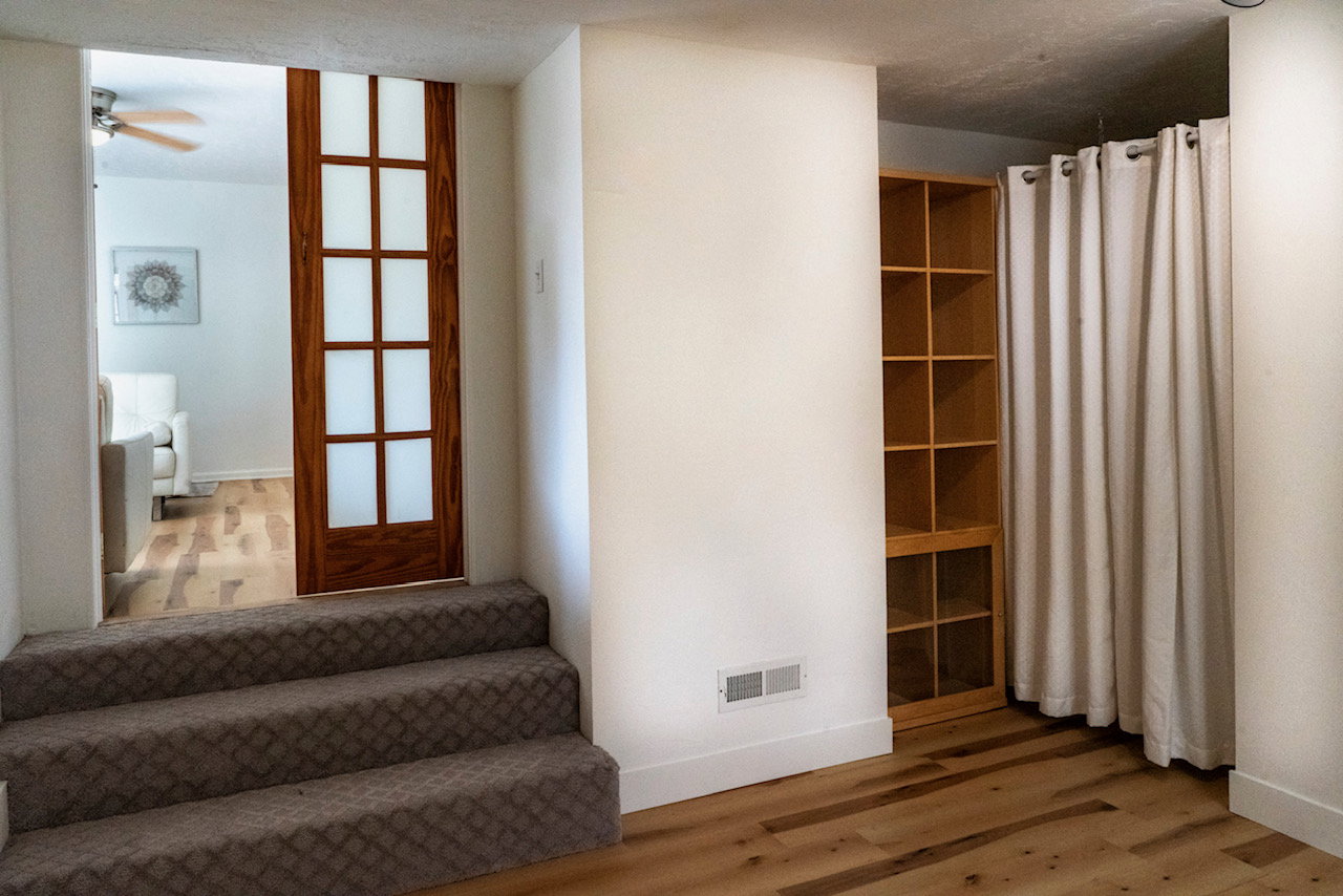 Sunken room featuring three carpeted steps, a wood-finish pocket door with frosted glass panels, and wood-finish flooring