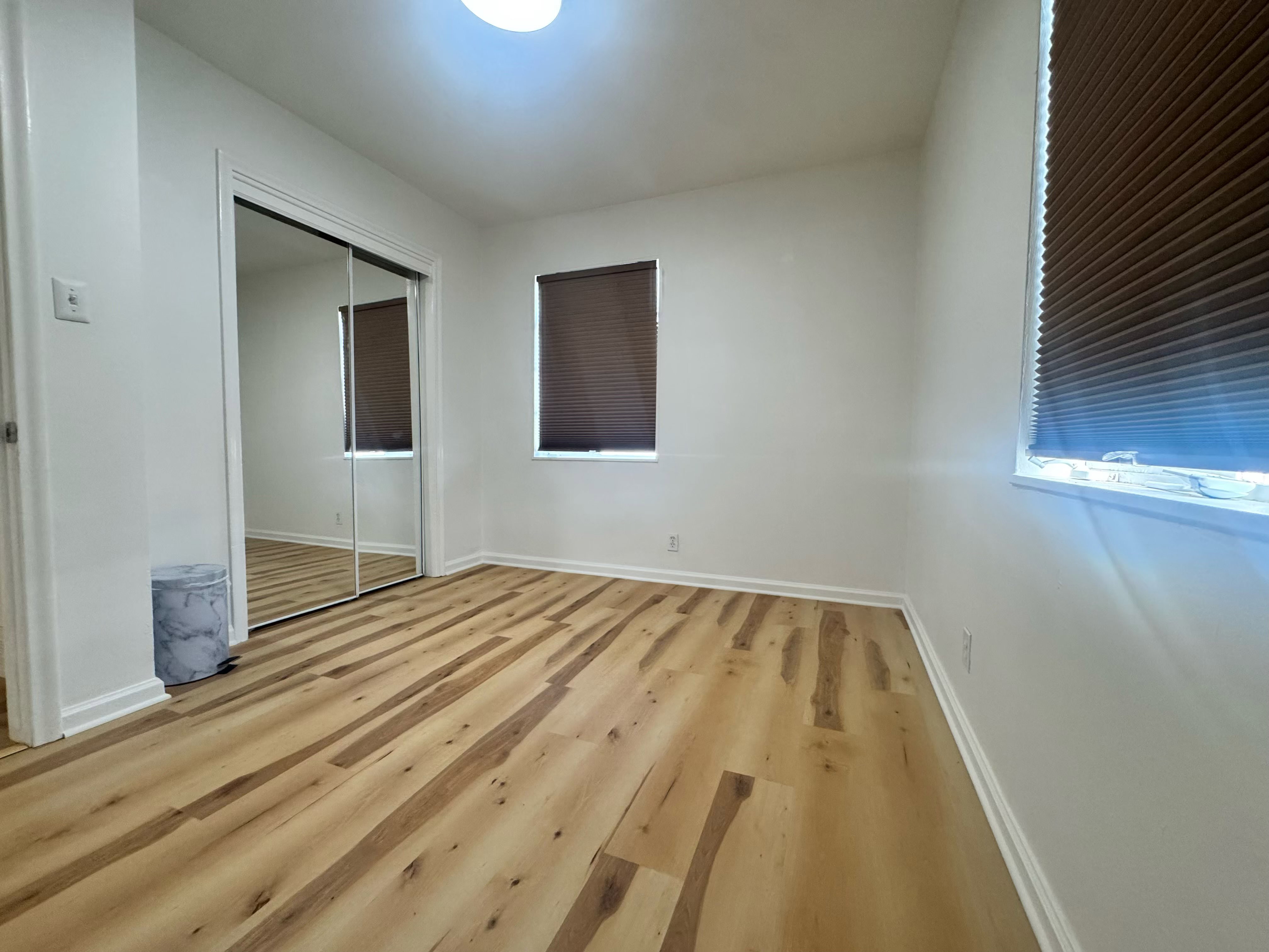 Bright interior space featuring wood-finish flooring, white walls, and two windows with brown blinds