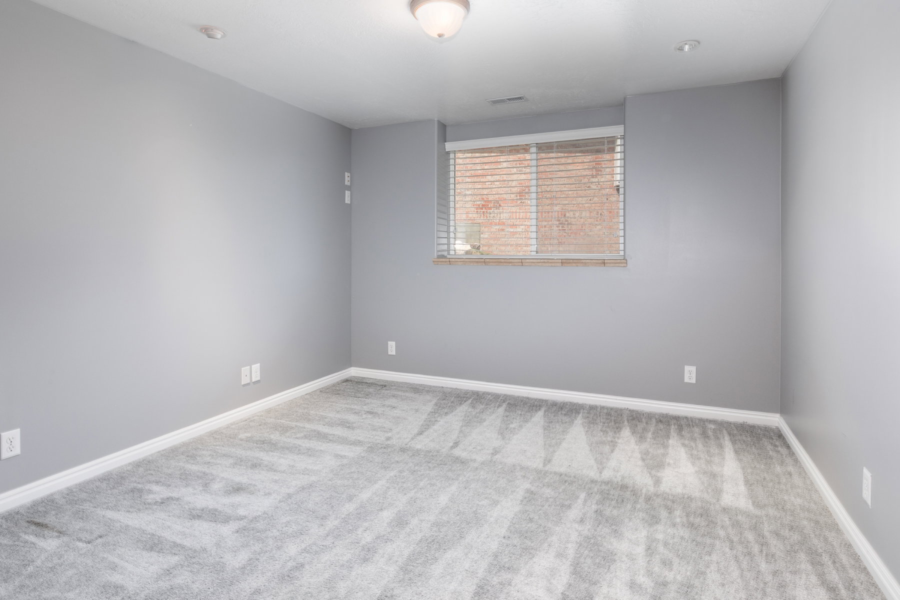 Gray patterned carpeting with white baseboards, a window featuring horizontal blinds, and a flush mount ceiling light