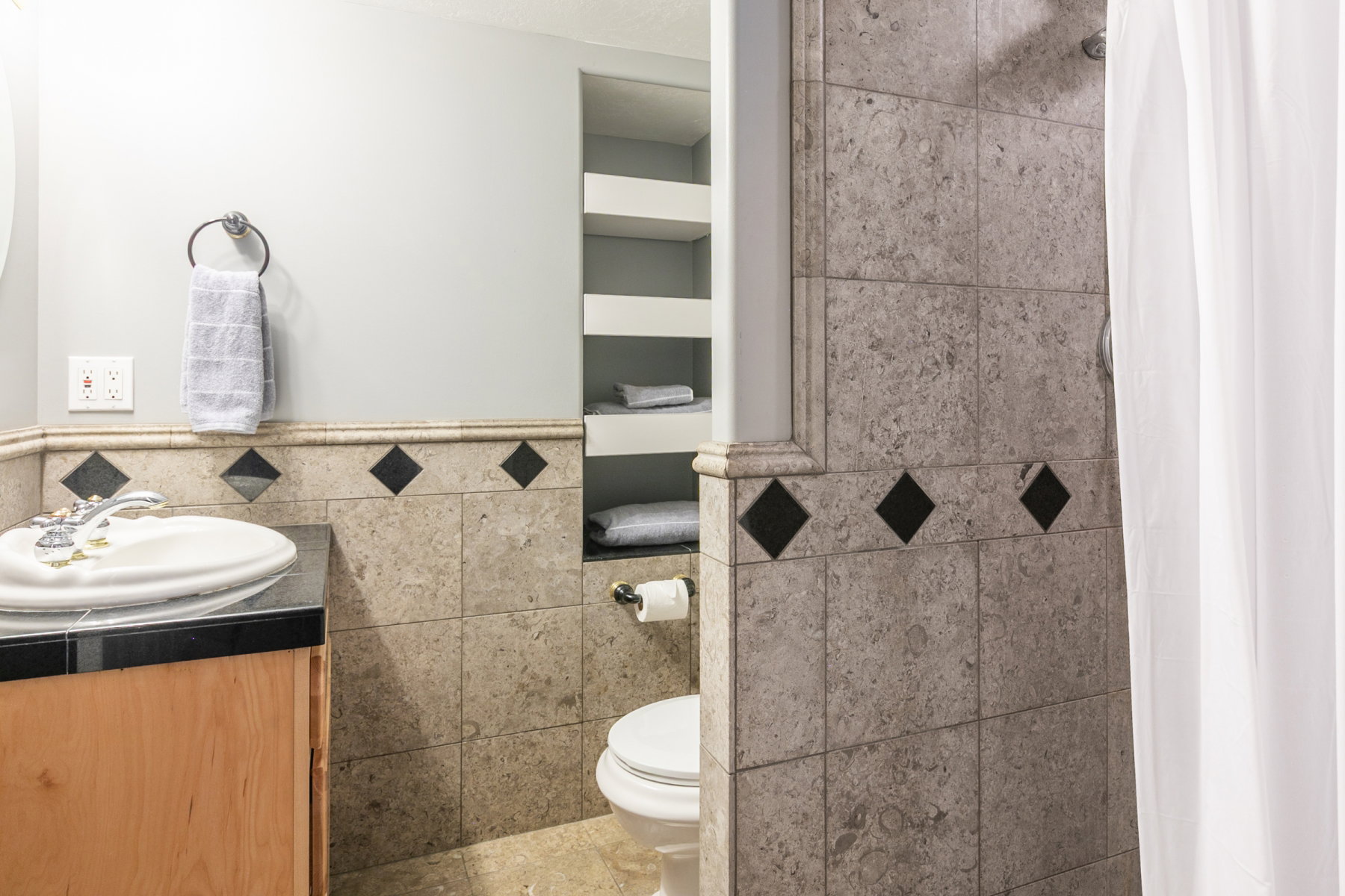 Tiled bathroom featuring a light wood-finish vanity with a black countertop and integrated sink