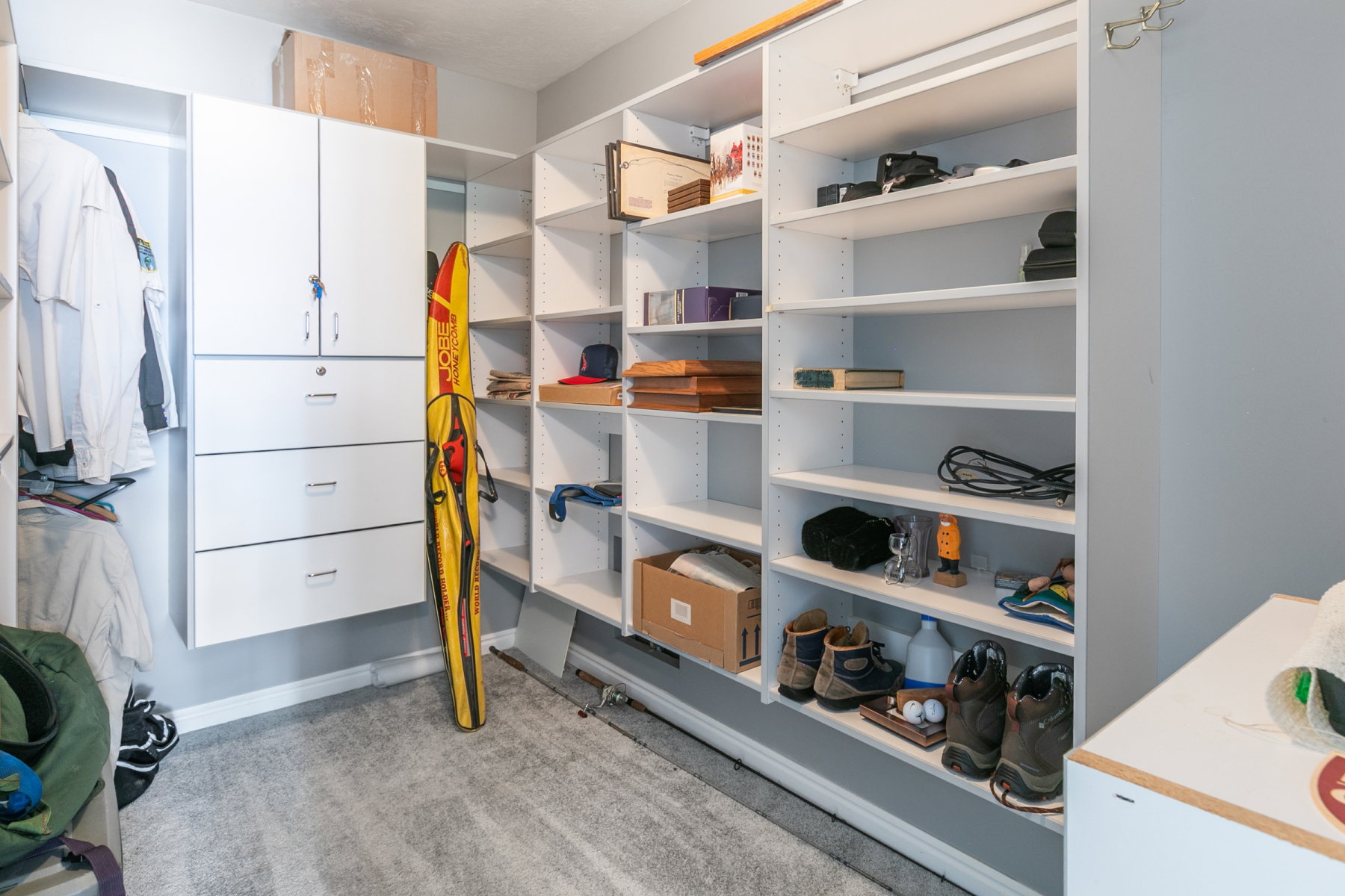 Custom closet system featuring extensive open shelving, a built-in cabinetry unit with locking doors, multiple drawers, and dedicated hanging space