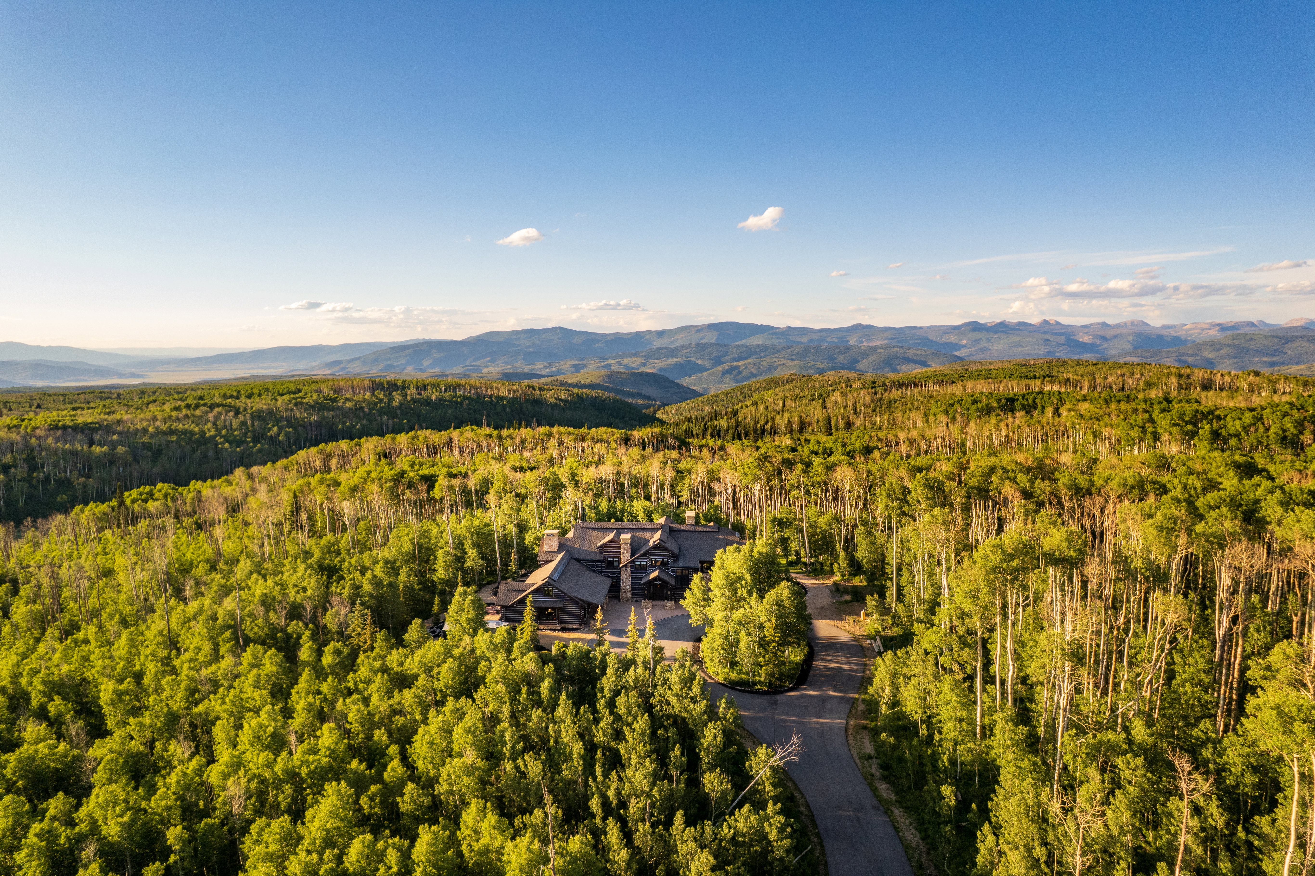 Custom home situated within a dense forest of mature trees, featuring a dark exterior facade and multiple rooflines