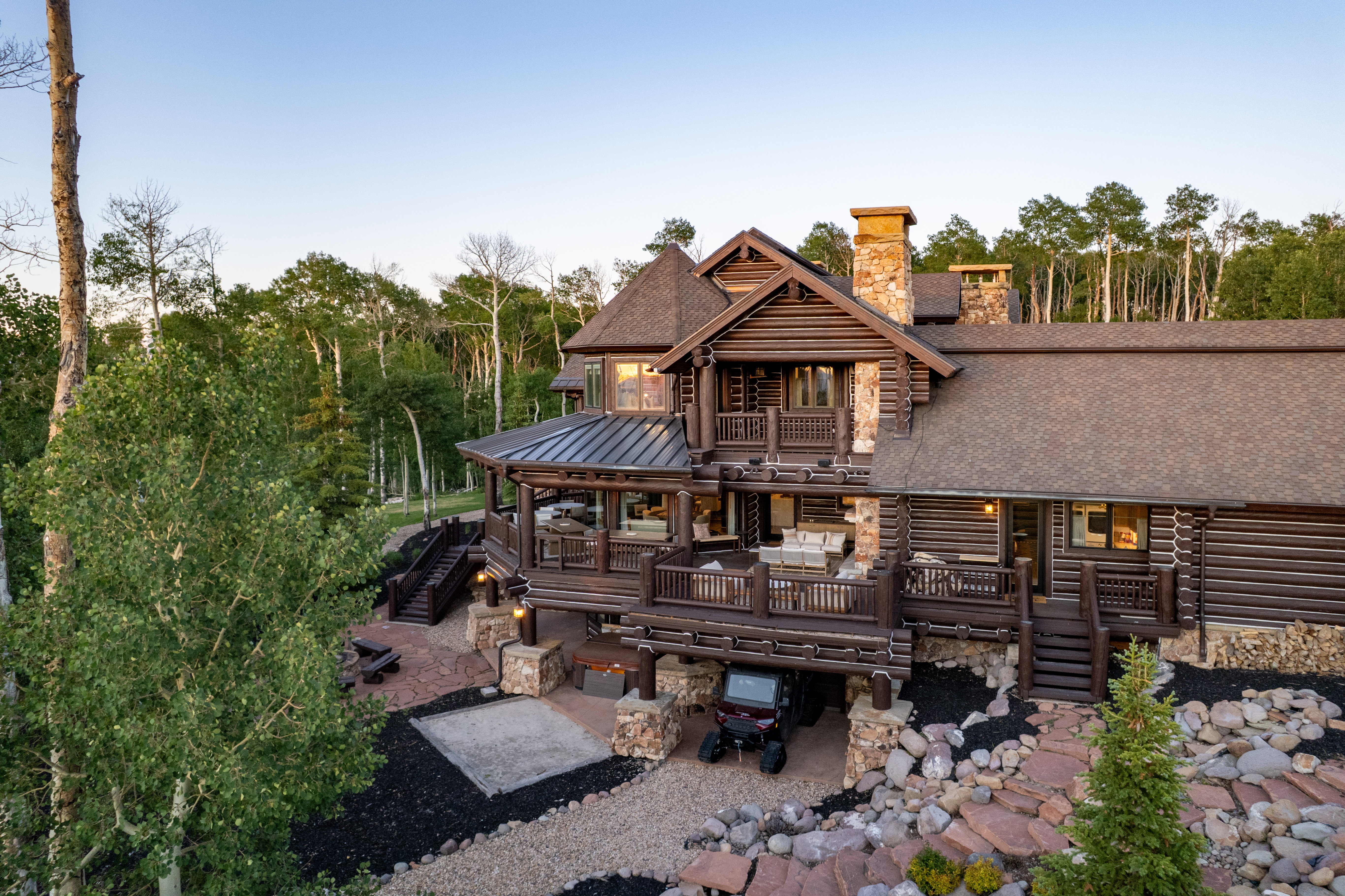 Log home exterior featuring multiple stone chimneys, expansive multi-level decking, and a gravel driveway