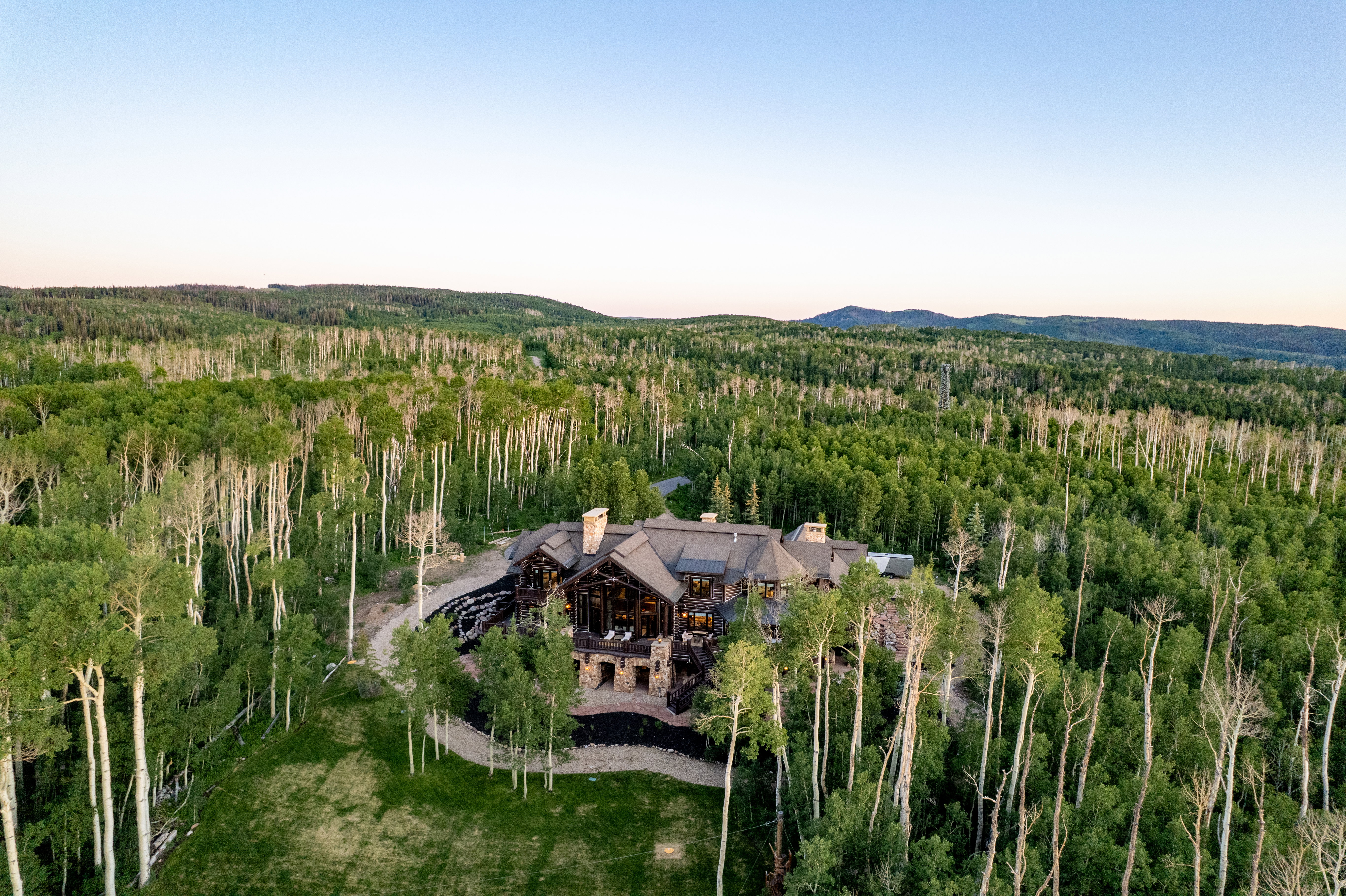 Sprawling woodland estate featuring a dark-toned multi-level residence with stone and wood siding, a stone chimney, and a multi-peaked roofline