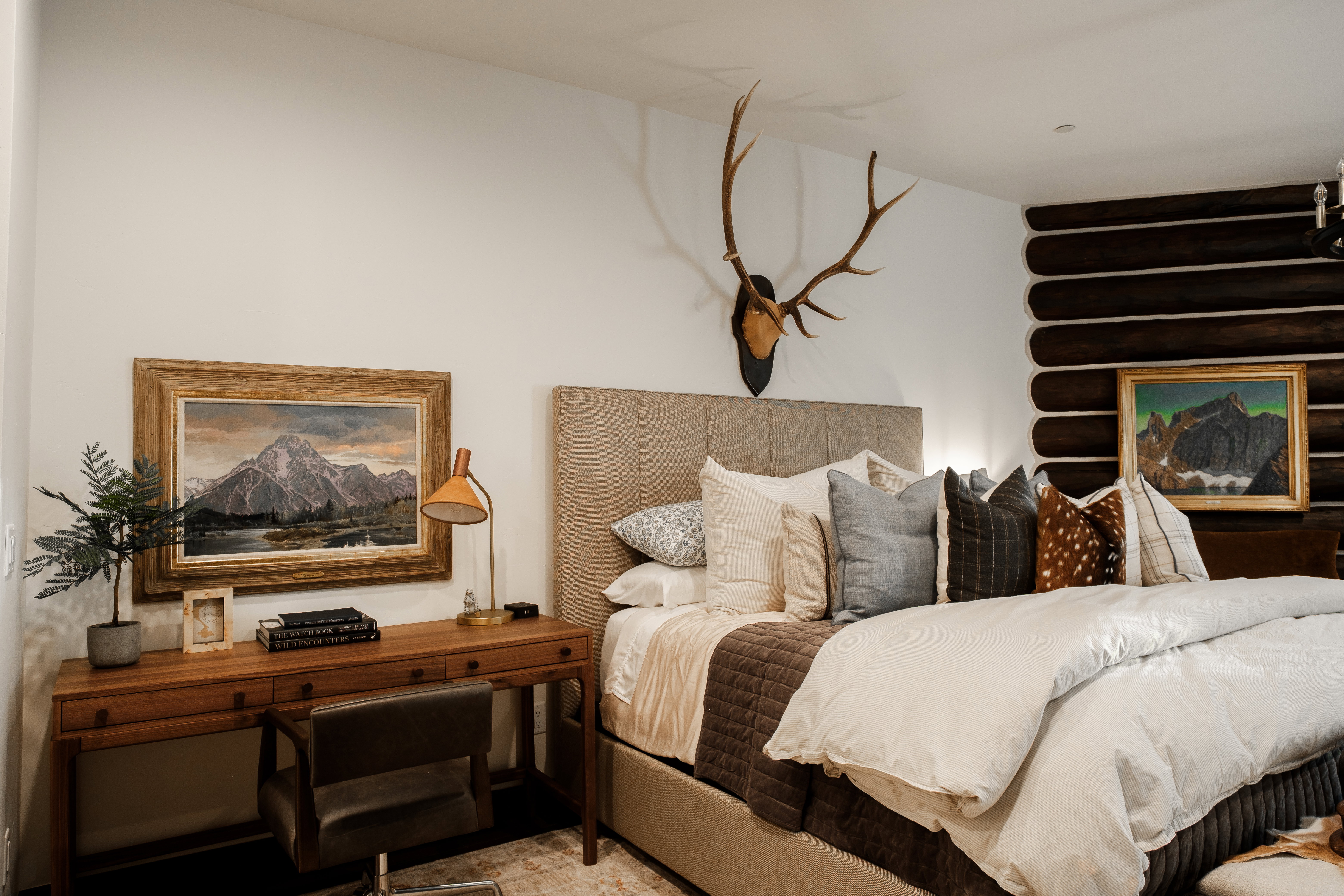 Bedroom featuring a beige upholstered headboard, a wood-finish desk, and a textured log wall detail