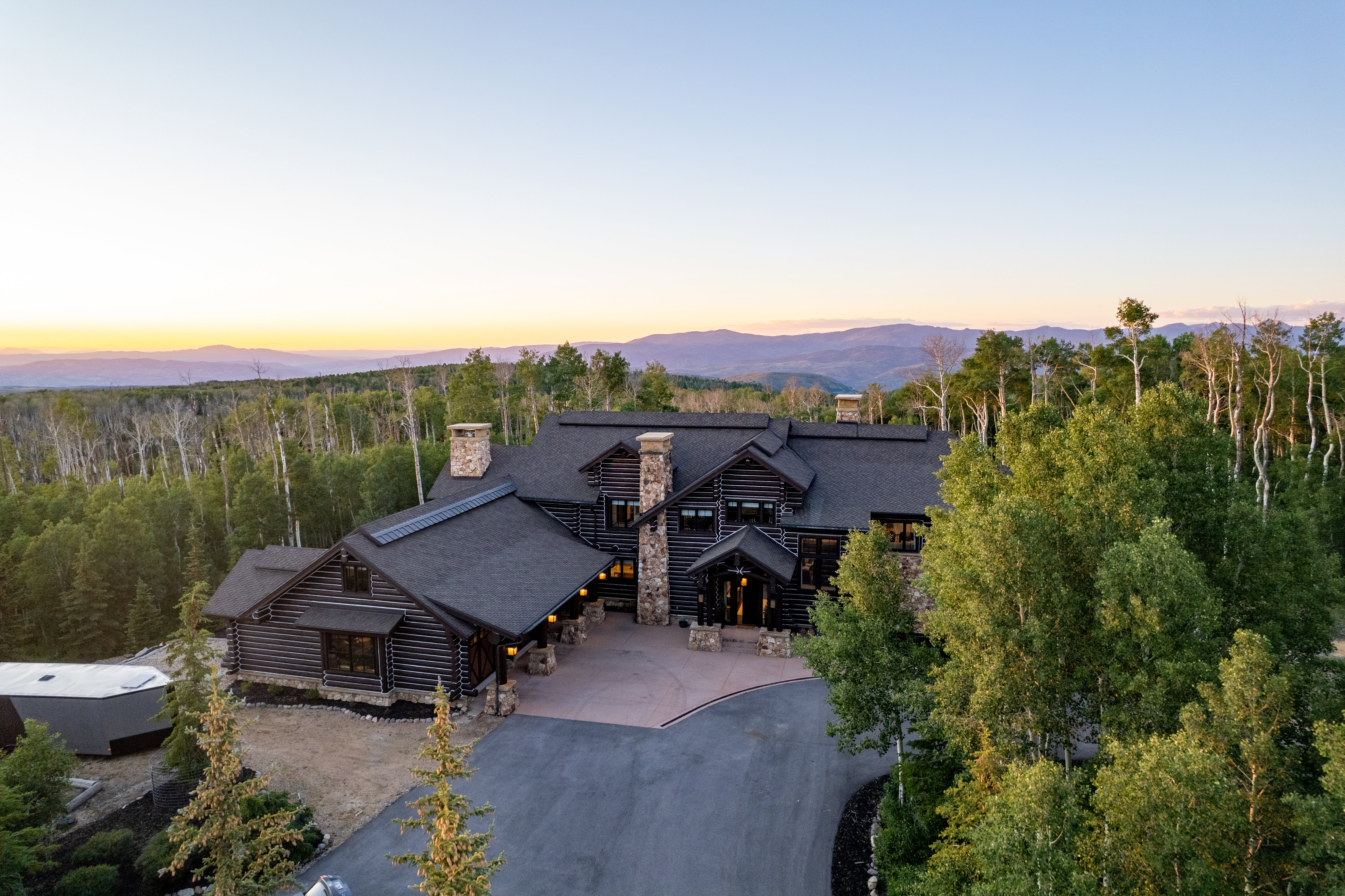 Log home with multiple stone chimneys and a dark shingle roof