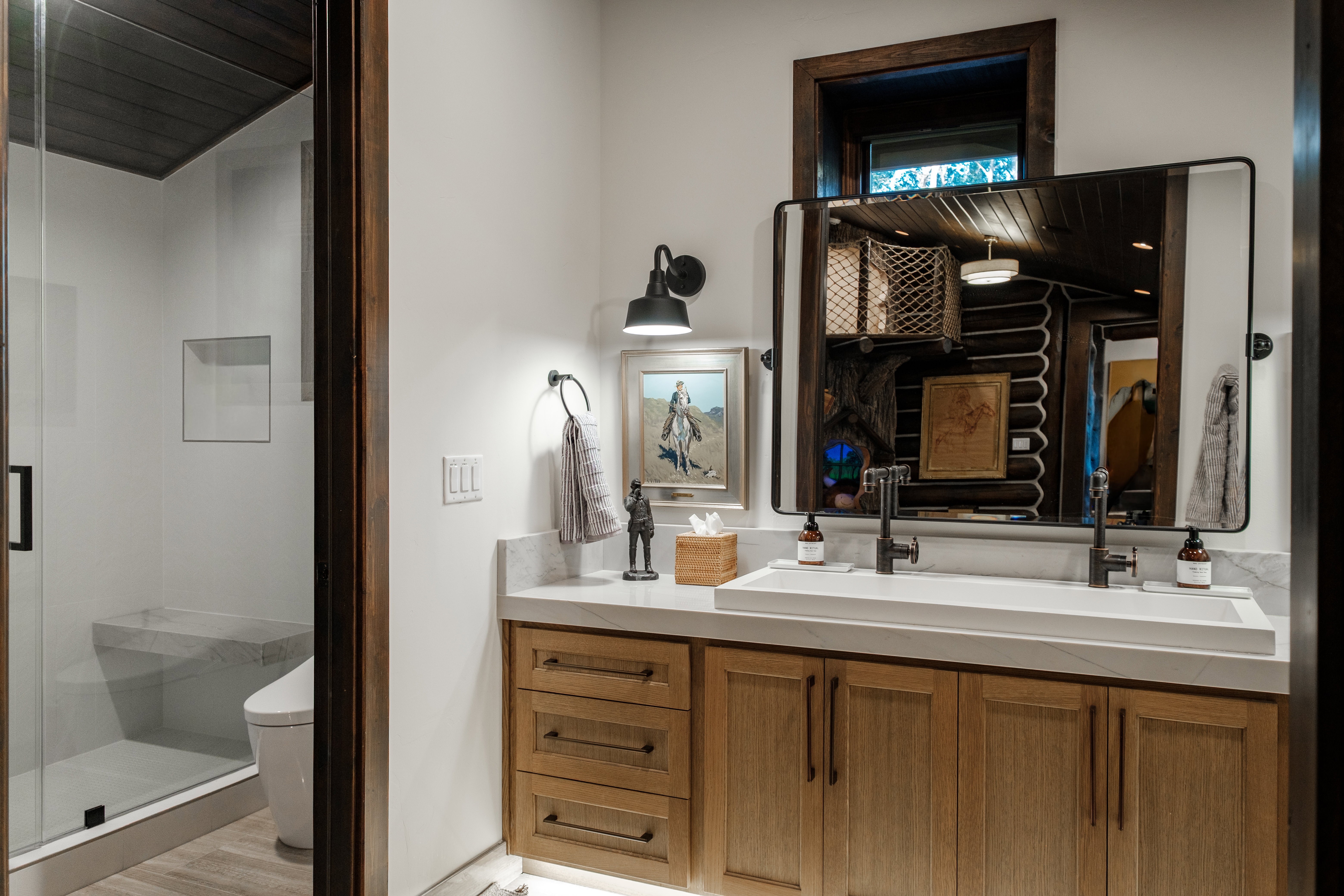 Contemporary bathroom featuring a light wood-finish double vanity with a rectangular integrated sink, matte black hardware, and a framed mirror