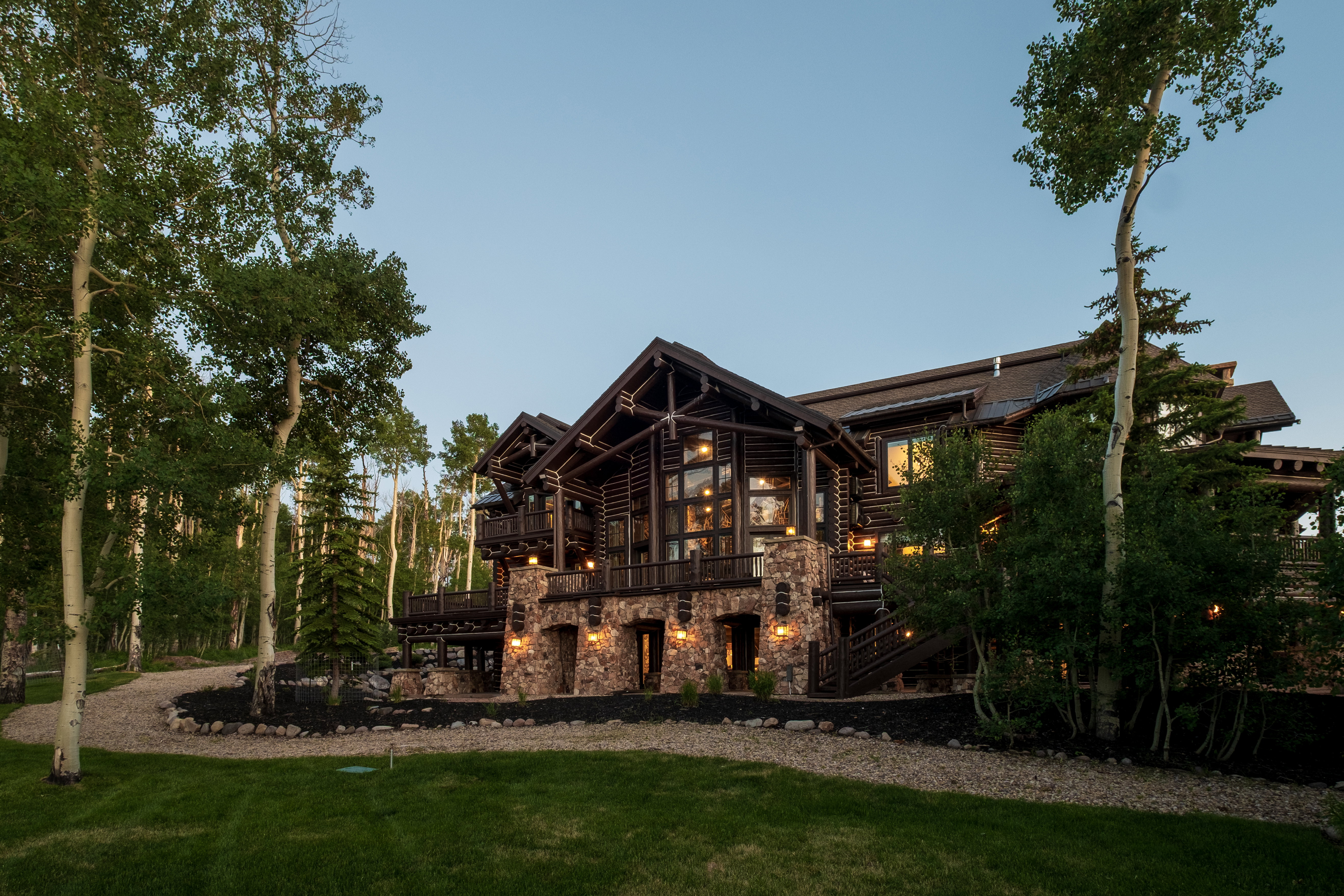 Multi-level log home featuring prominent stone accents, extensive exterior lighting, and multiple balconies