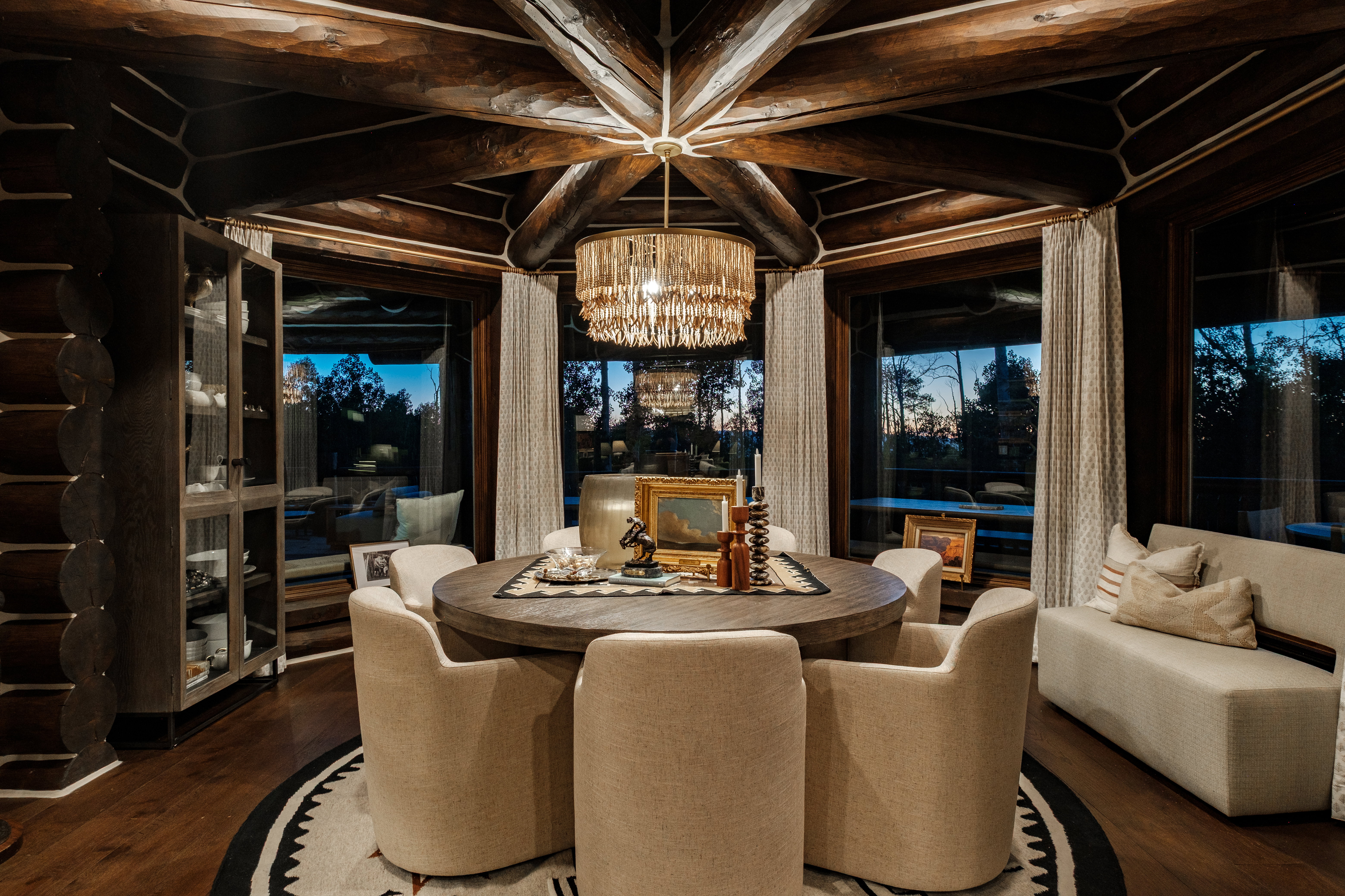 Dining area featuring exposed log and timber beam ceiling, a round wood-finish dining table, and dark wood-finish flooring