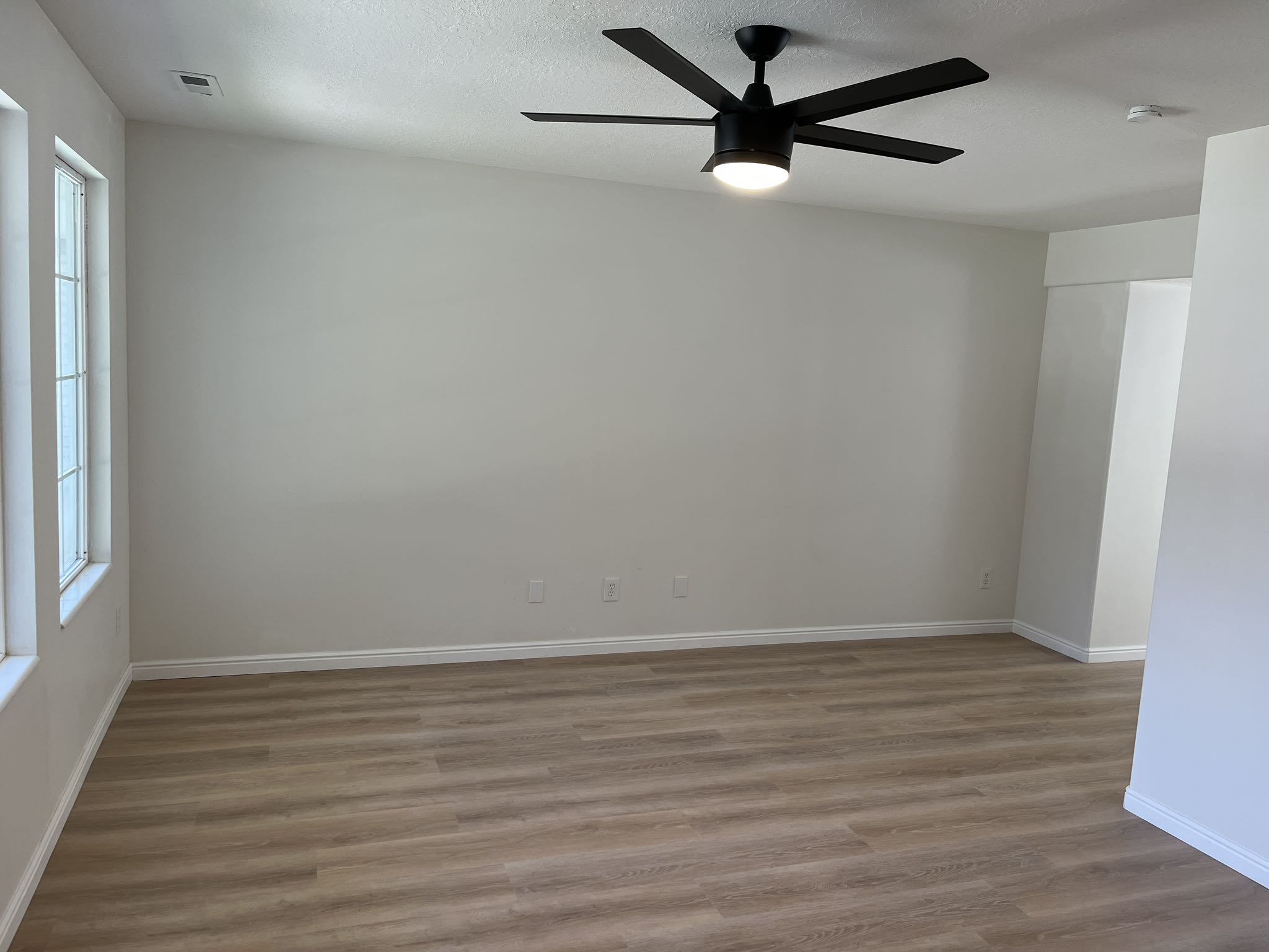 Spacious interior featuring wood-finish flooring, white baseboards, and a contemporary black ceiling fan with integrated lighting