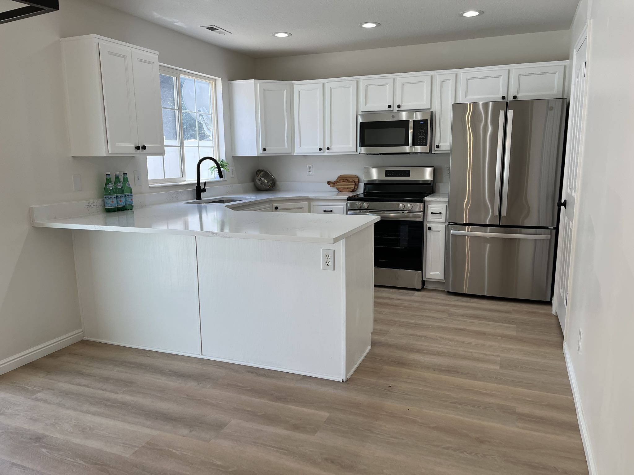 Modern kitchen featuring white shaker cabinetry, stainless steel appliances, light wood-finish flooring, recessed lighting, and a breakfast bar with solid surface countertops