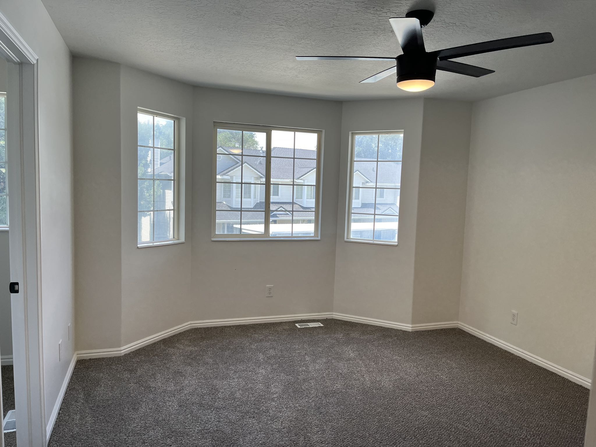Carpeted room featuring a bay window with three multi-pane windows, a contemporary ceiling fan with integrated lighting, and white baseboards