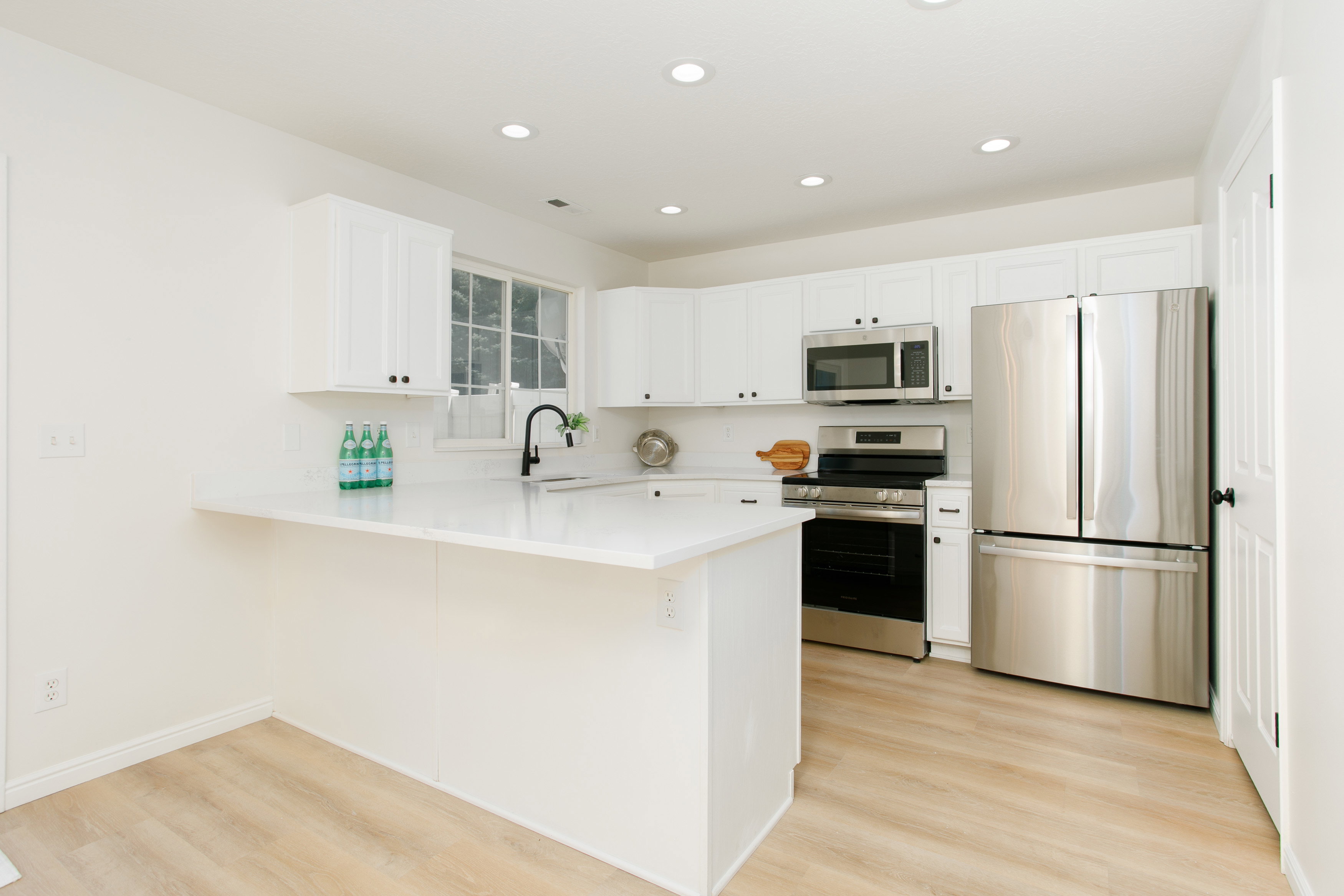 Bright kitchen featuring white shaker cabinetry, stainless steel appliances, light wood-finish flooring, recessed lighting, and a white countertop with an undermount sink