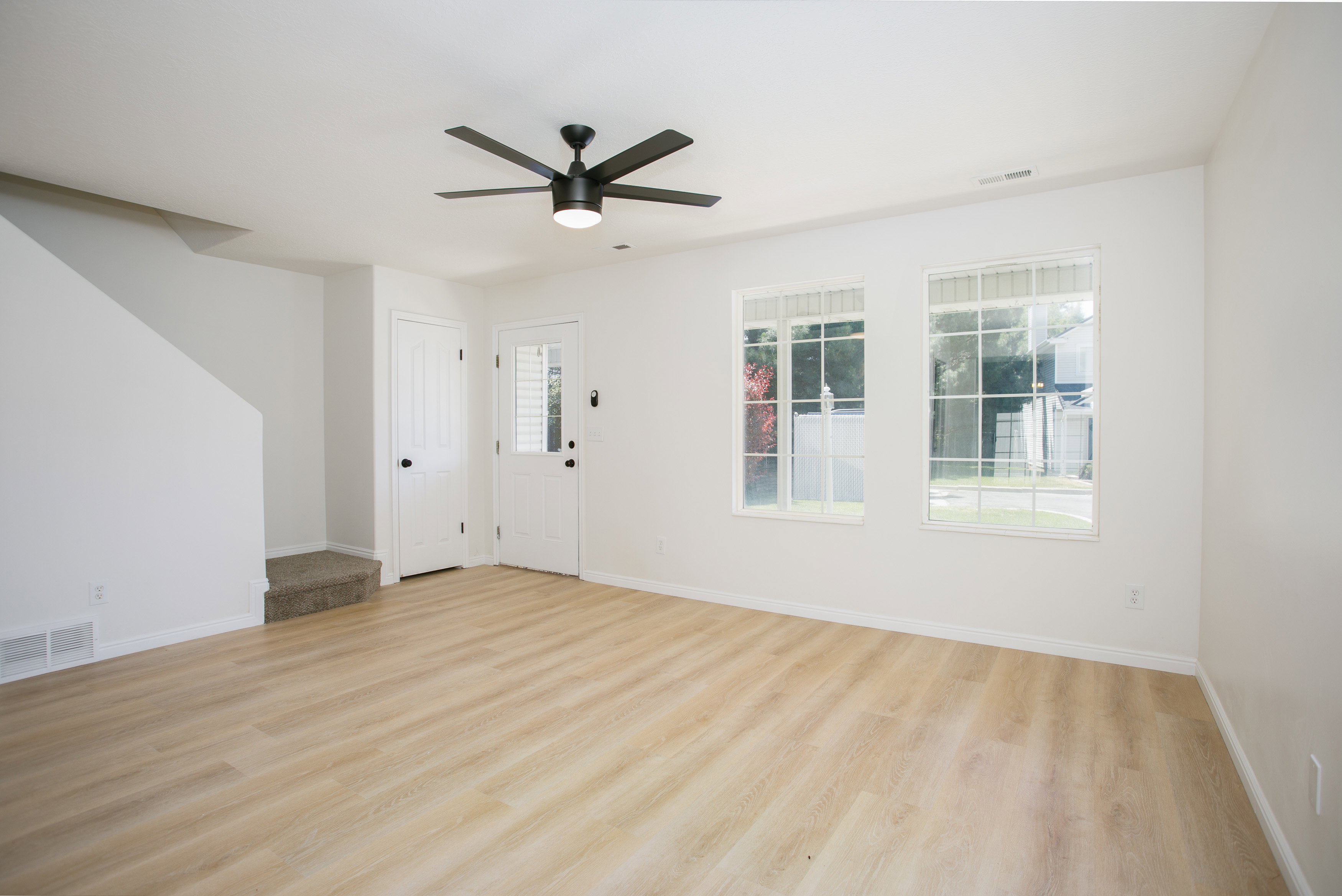 Spacious room featuring light wood-finish flooring, white walls, and a contemporary ceiling fan