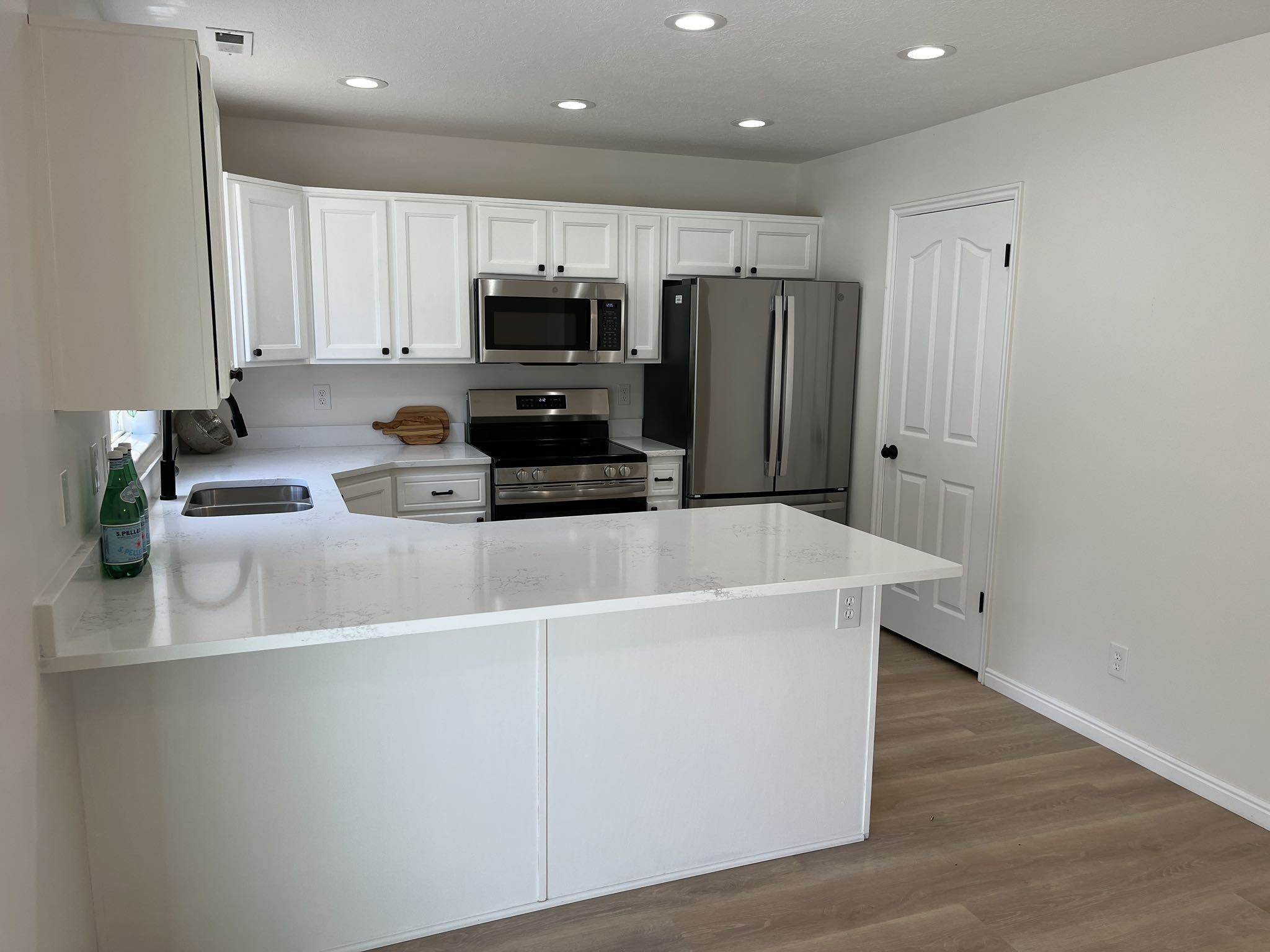 Modern kitchen featuring white shaker cabinetry, stainless steel appliances, light-toned countertops, wood-finish flooring, and recessed lighting