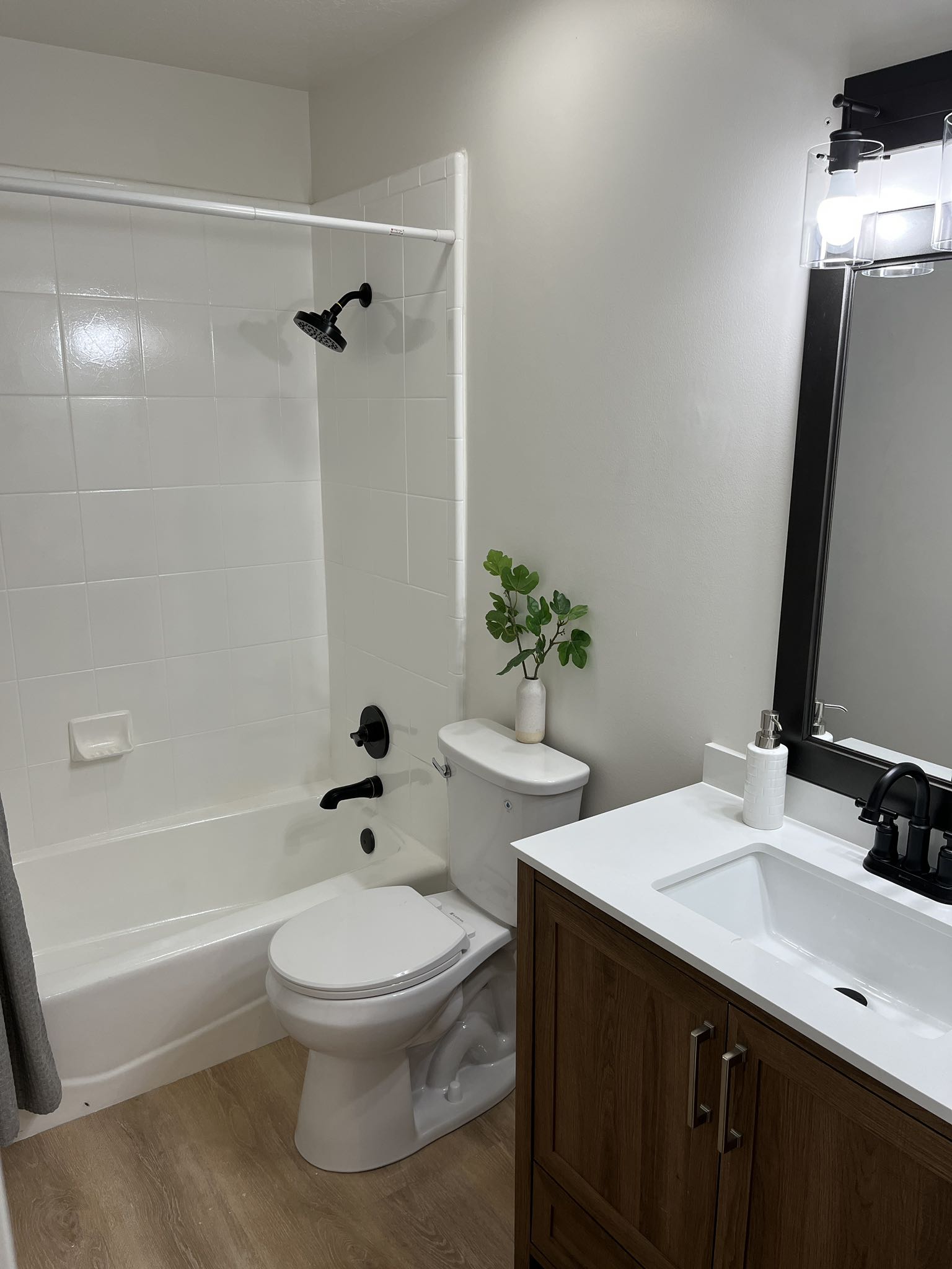 Bathroom featuring a white subway tile shower surround with matte black fixtures, a white porcelain bathtub, and a wood-finish vanity with a white countertop and integrated sink