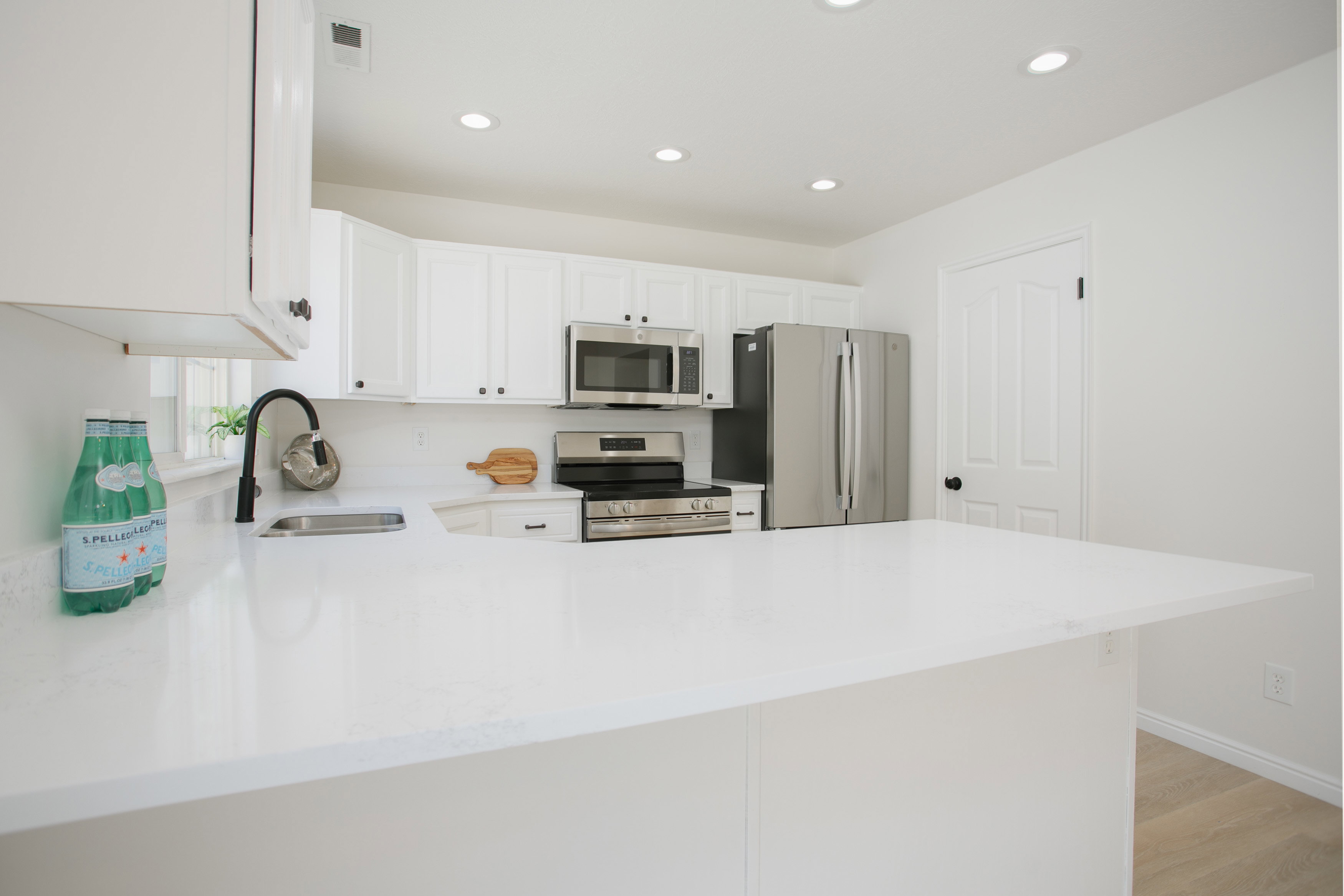 Kitchen featuring white cabinetry, stainless steel appliances, a white tile backsplash, and a large white countertop with a sink and a black faucet