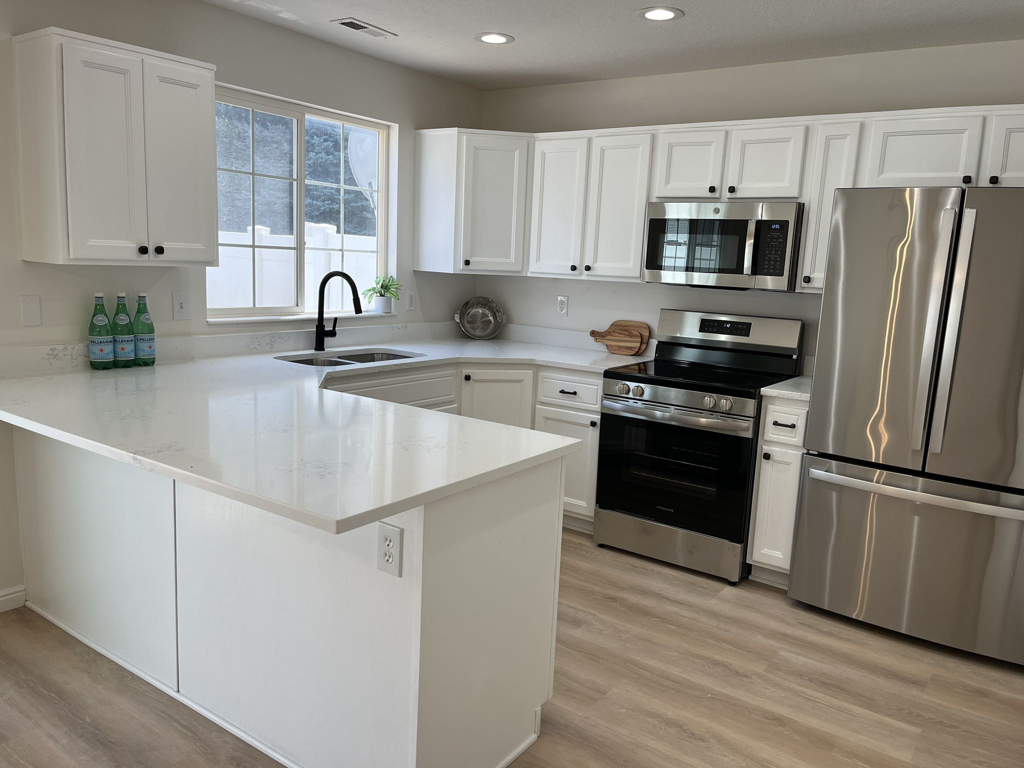 Modern kitchen featuring white cabinetry, light-toned countertops, stainless steel appliances, a black gooseneck faucet, and wood-finish flooring