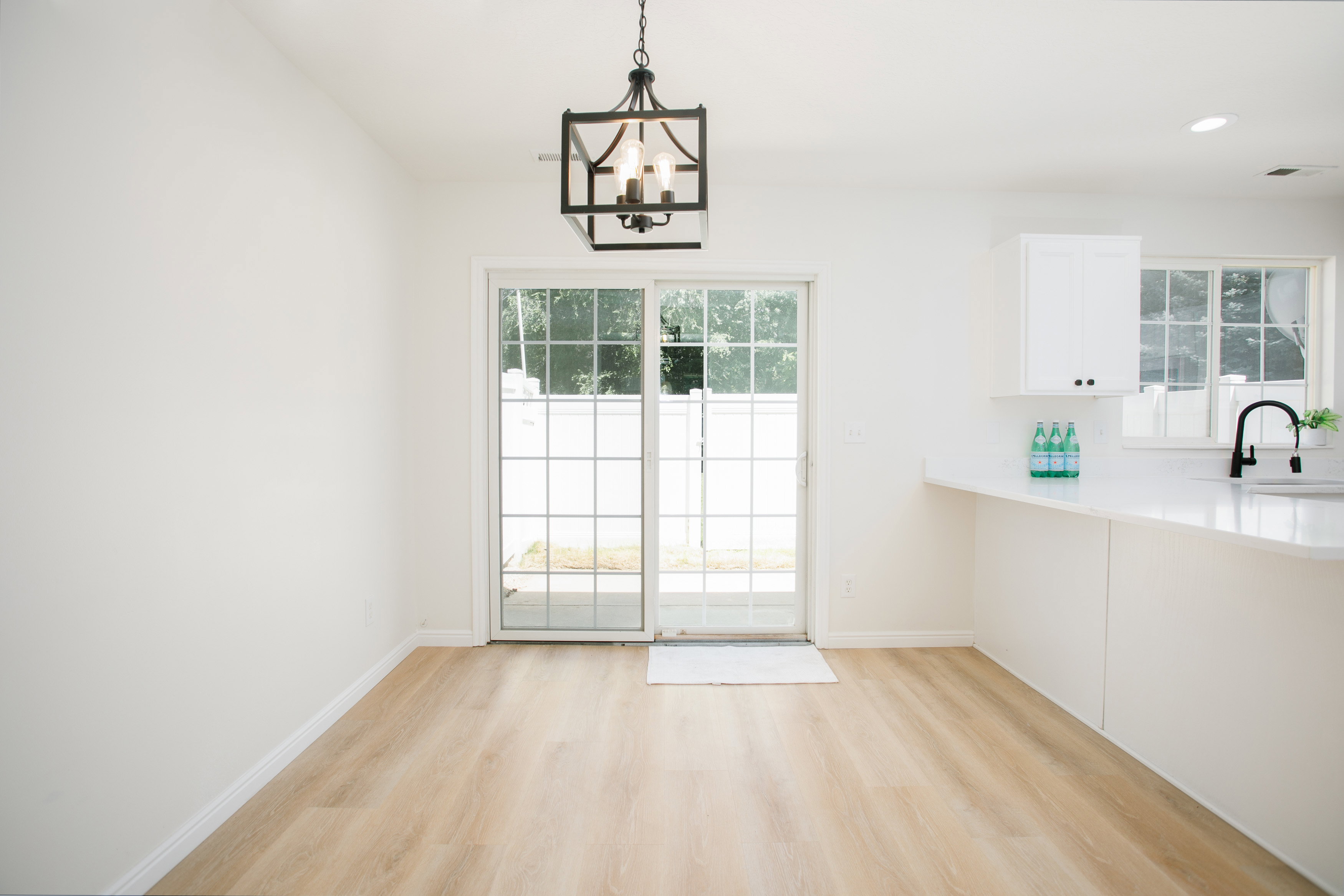 Open-concept area featuring light wood-finish flooring, a contemporary black pendant light fixture, and white walls