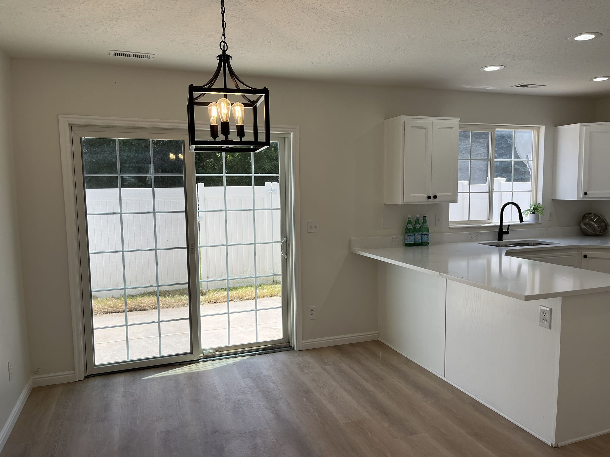 Open-concept dining area featuring a modern black chandelier, wood-finish flooring, and sliding glass doors to the outdoor patio