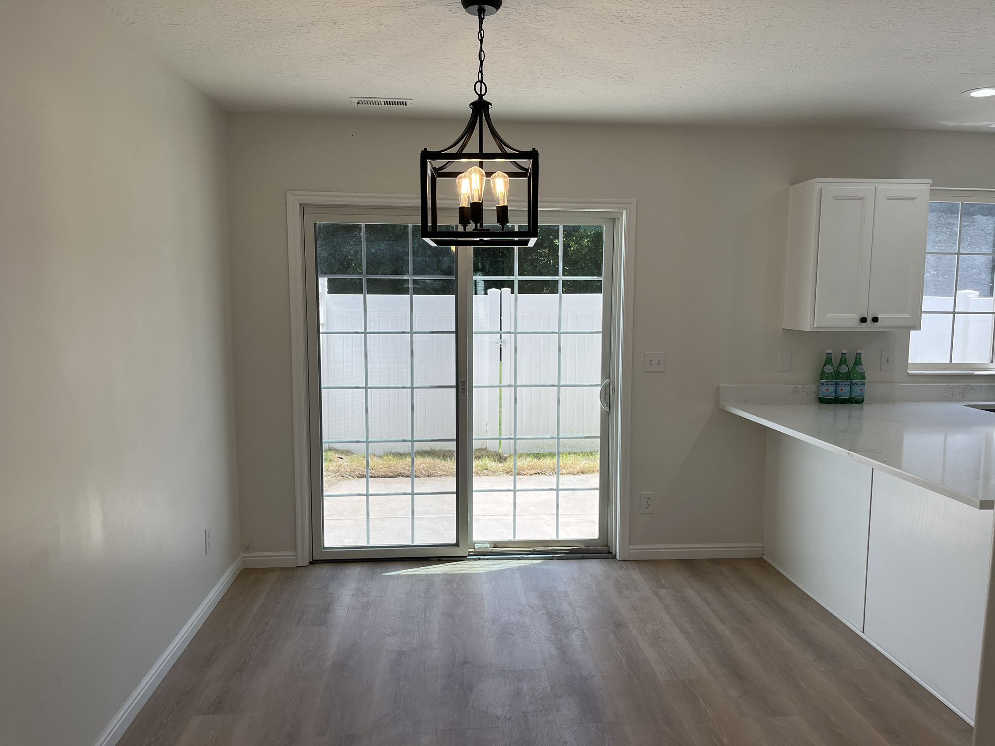 Open-concept room featuring wood-finish flooring, a contemporary black metal chandelier, and a sliding glass door with grid patterns leading to an outdoor paved area