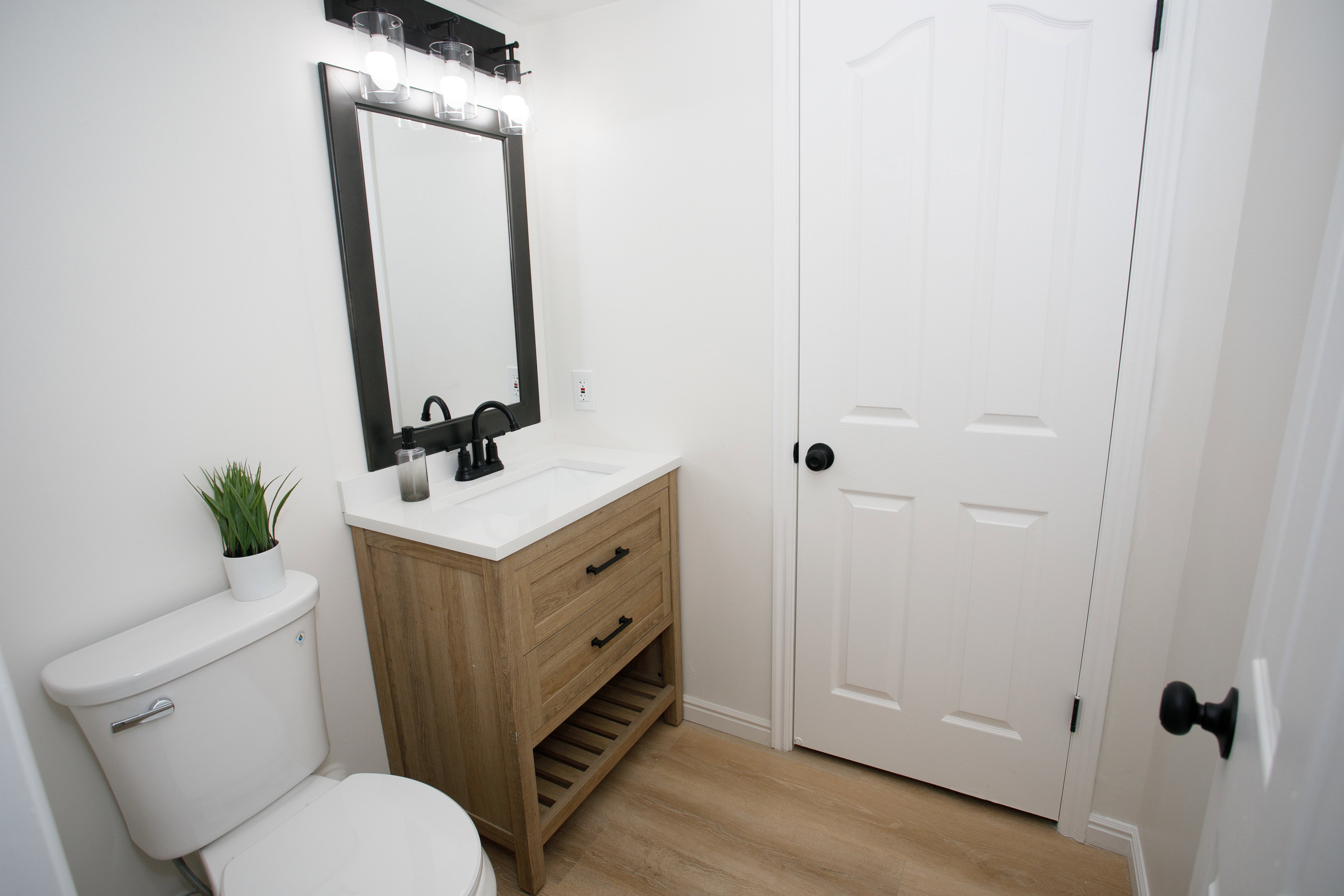 Modern bathroom featuring a wood-finish vanity with a white countertop and integrated sink, matte black faucet, and a coordinating framed mirror