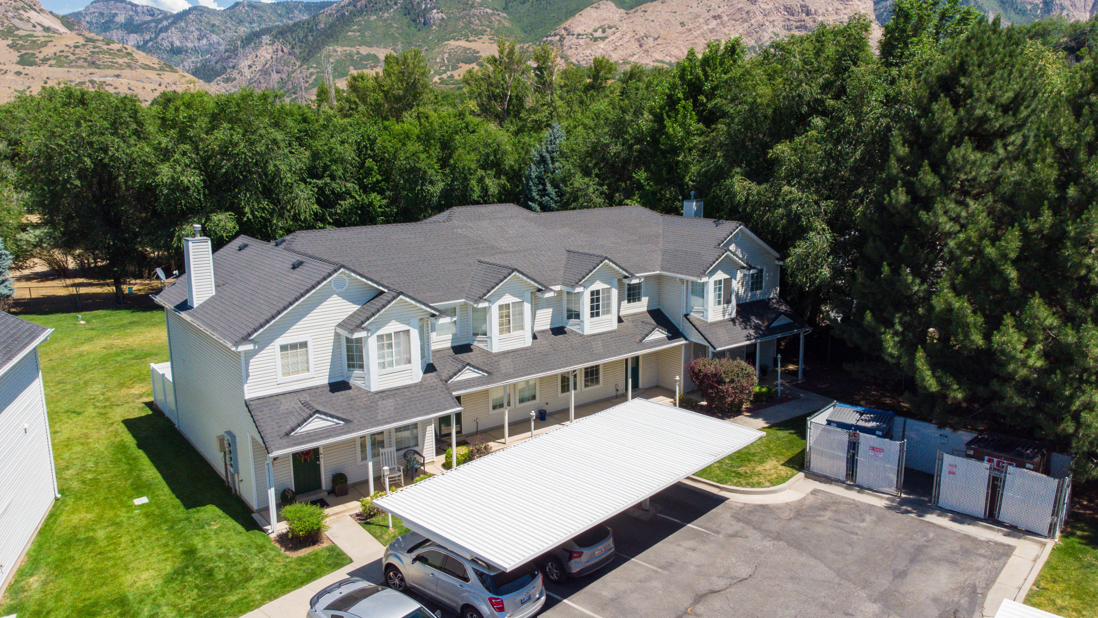 Multi-unit residential property featuring a gray shingled roof, white siding, and multiple dormer windows