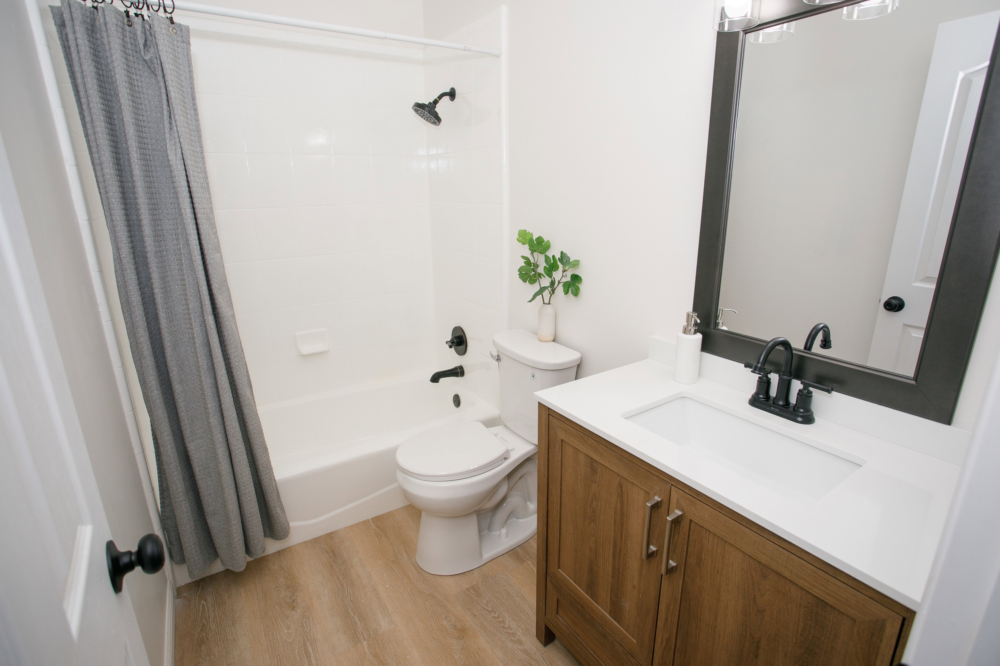 White bathroom featuring a single vanity with wood-finish cabinetry, a white countertop, and a black framed mirror