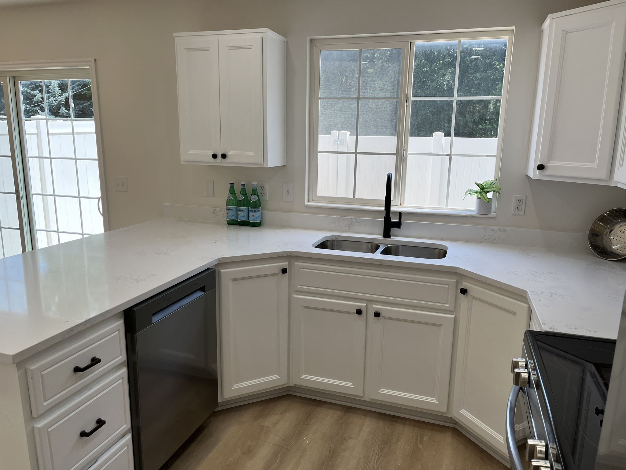Kitchen featuring white cabinetry with black hardware, light-toned countertops, a dual basin stainless steel sink with a black faucet, and stainless steel appliances