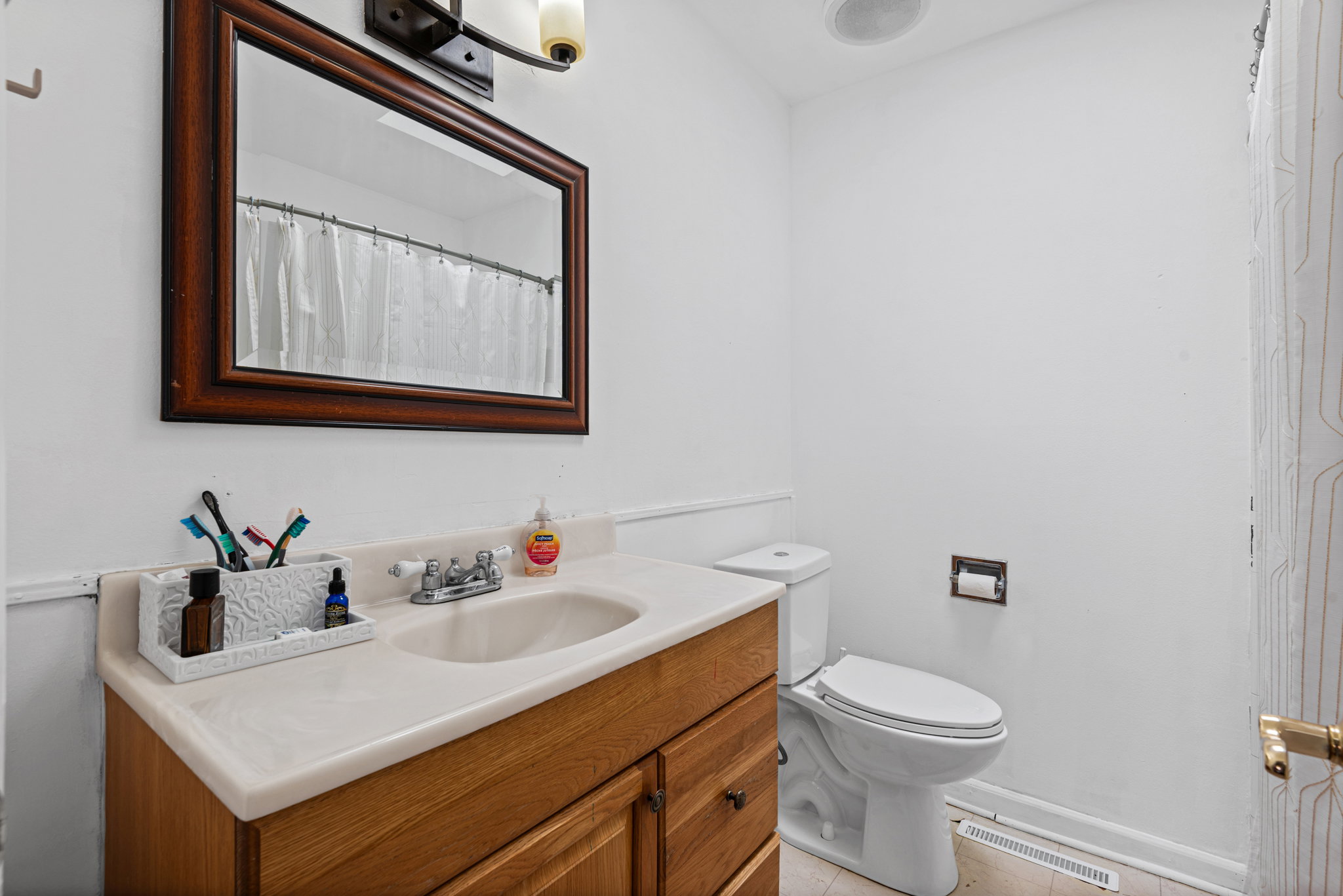 Full bathroom featuring a wood-finish vanity with an integrated sink, a large framed mirror, and white wall paneling