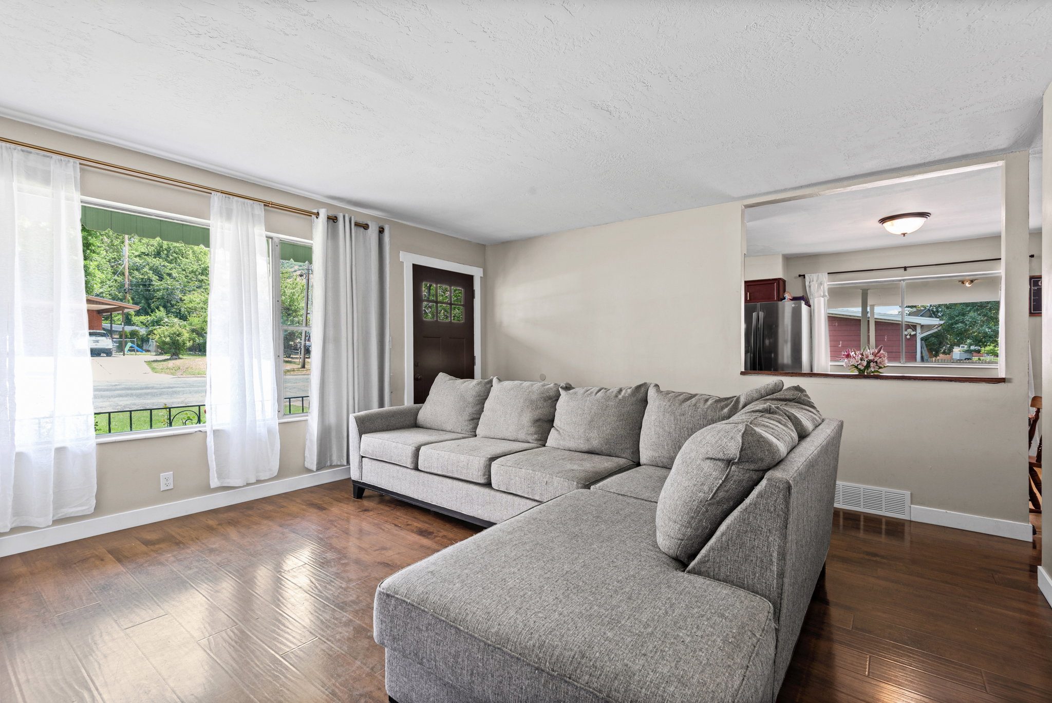 Spacious living area featuring wood-finish flooring, multiple windows, and a partial wall opening to an additional room