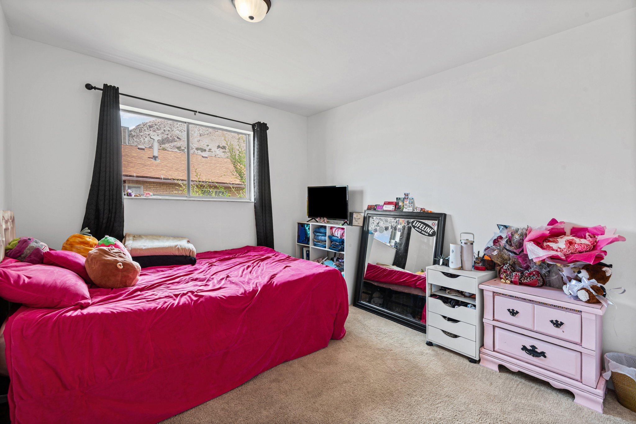 Carpeted bedroom featuring a single window with dark drapery, white walls, and a ceiling-mounted light fixture