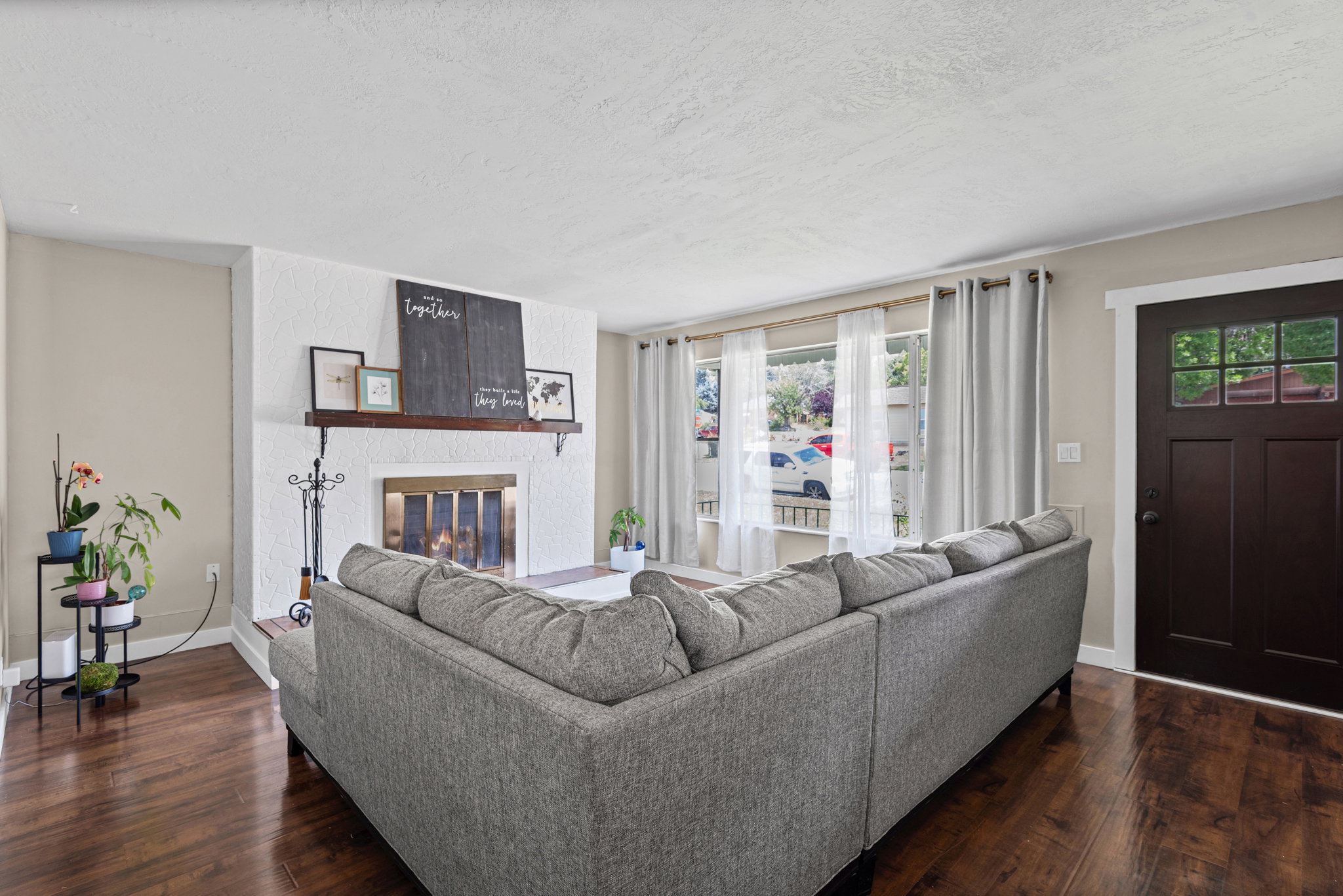 Living area featuring wood-finish flooring, a white textured fireplace, a dark wood mantel, and large picture windows