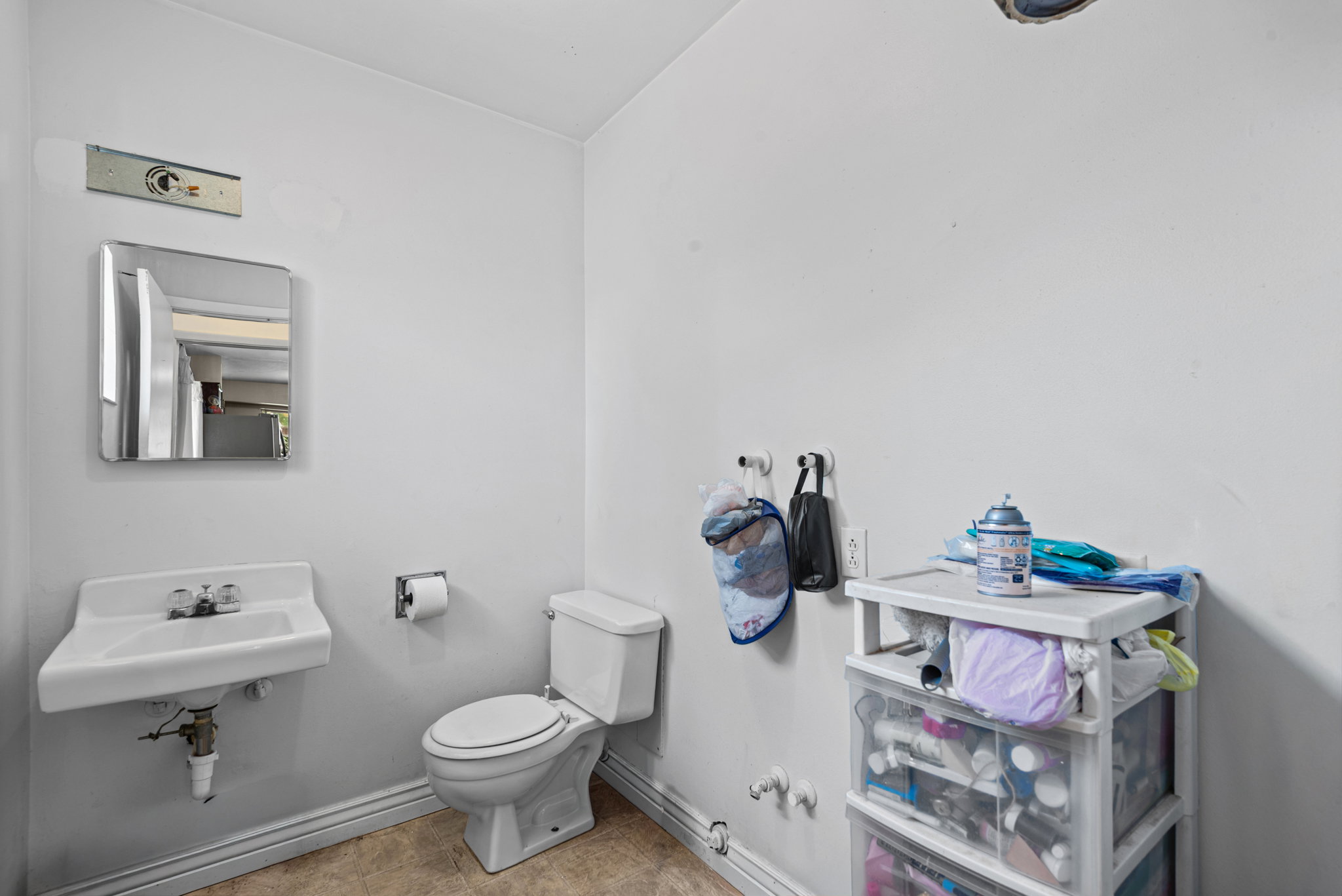 Bathroom featuring a wall-mounted sink, a toilet, a wall-mounted mirror, and neutral wall paint