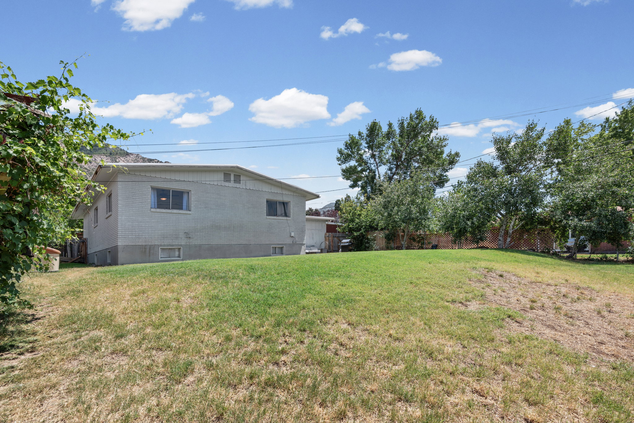 Spacious grassy yard with mature trees and a partial mountain backdrop