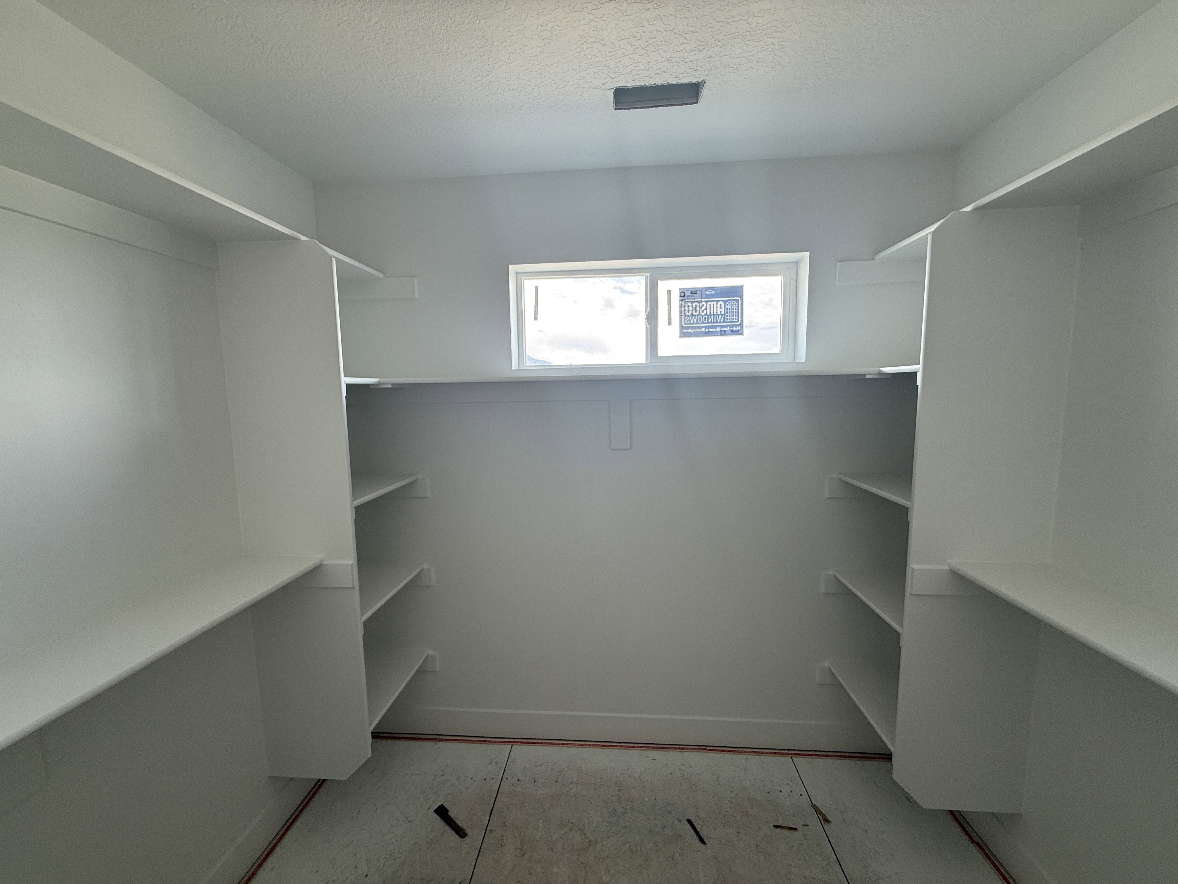 Spacious walk-in closet featuring white built-in shelving, hanging rods, and a window for natural light