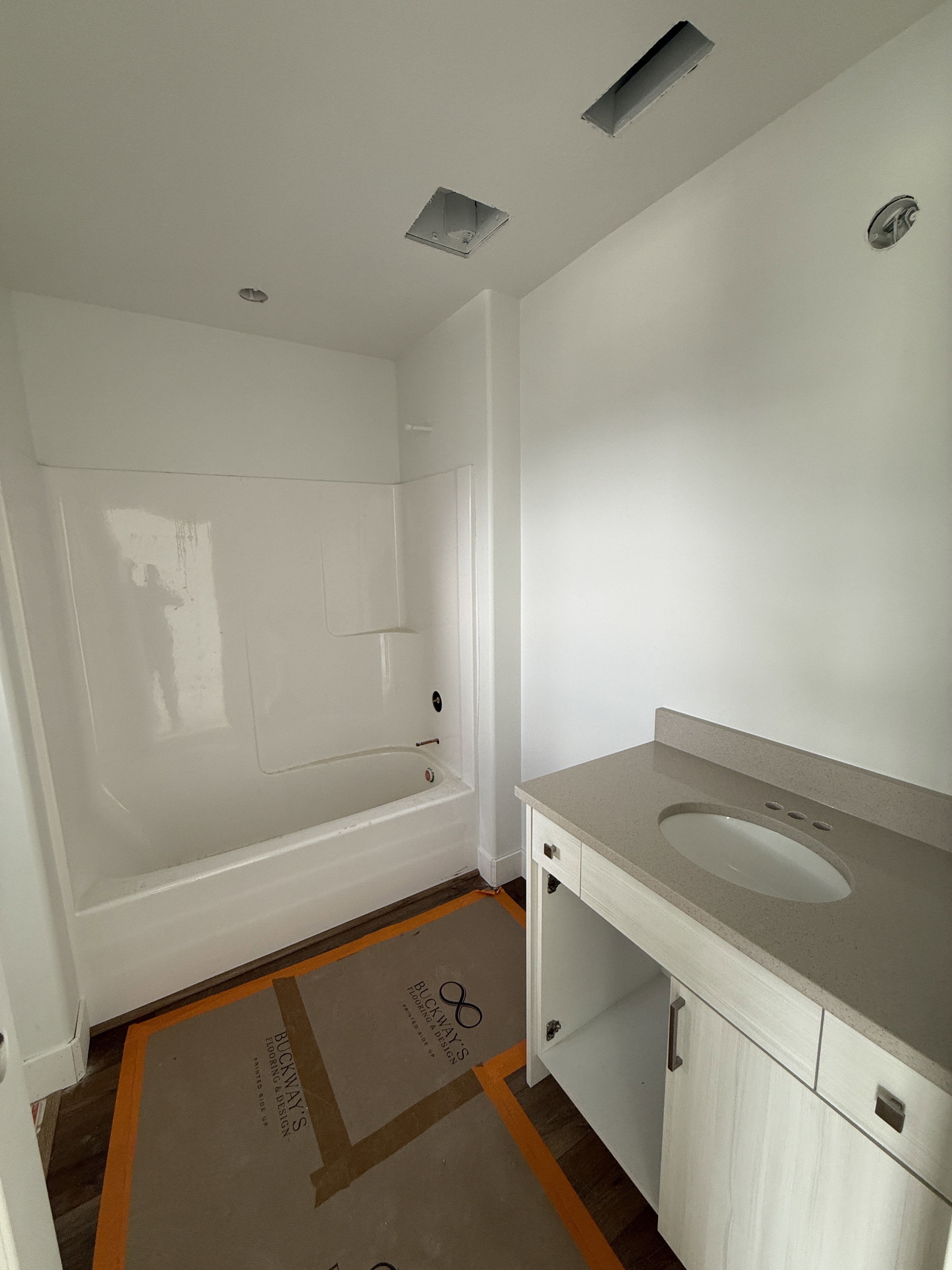 Contemporary bathroom featuring a combined tub and shower unit, wood-finish flooring, a light-toned vanity with a built-in sink, and a complementing countertop