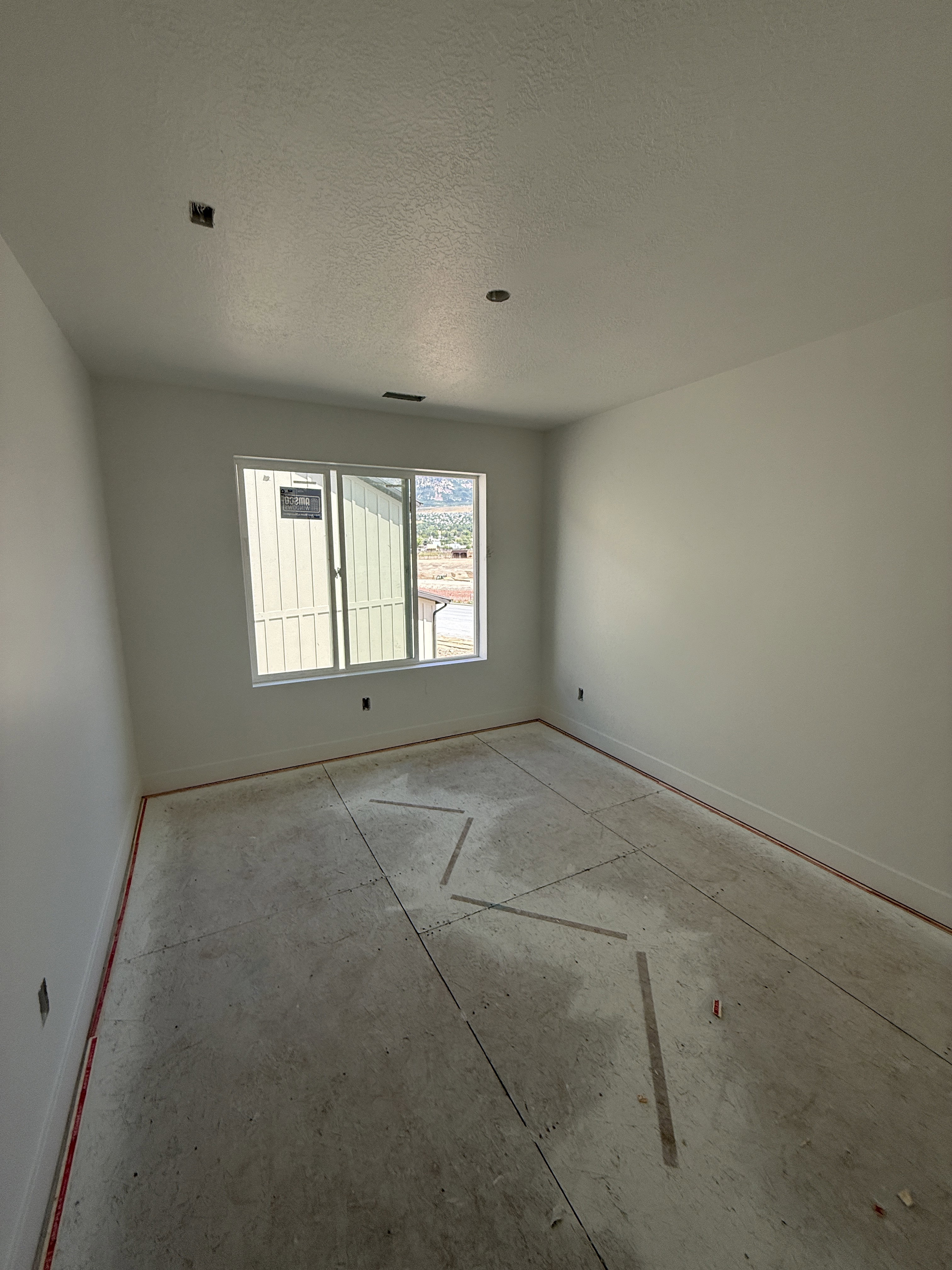 Light-filled room featuring a large window, neutral wall paint, and unfinished subflooring ready for customization