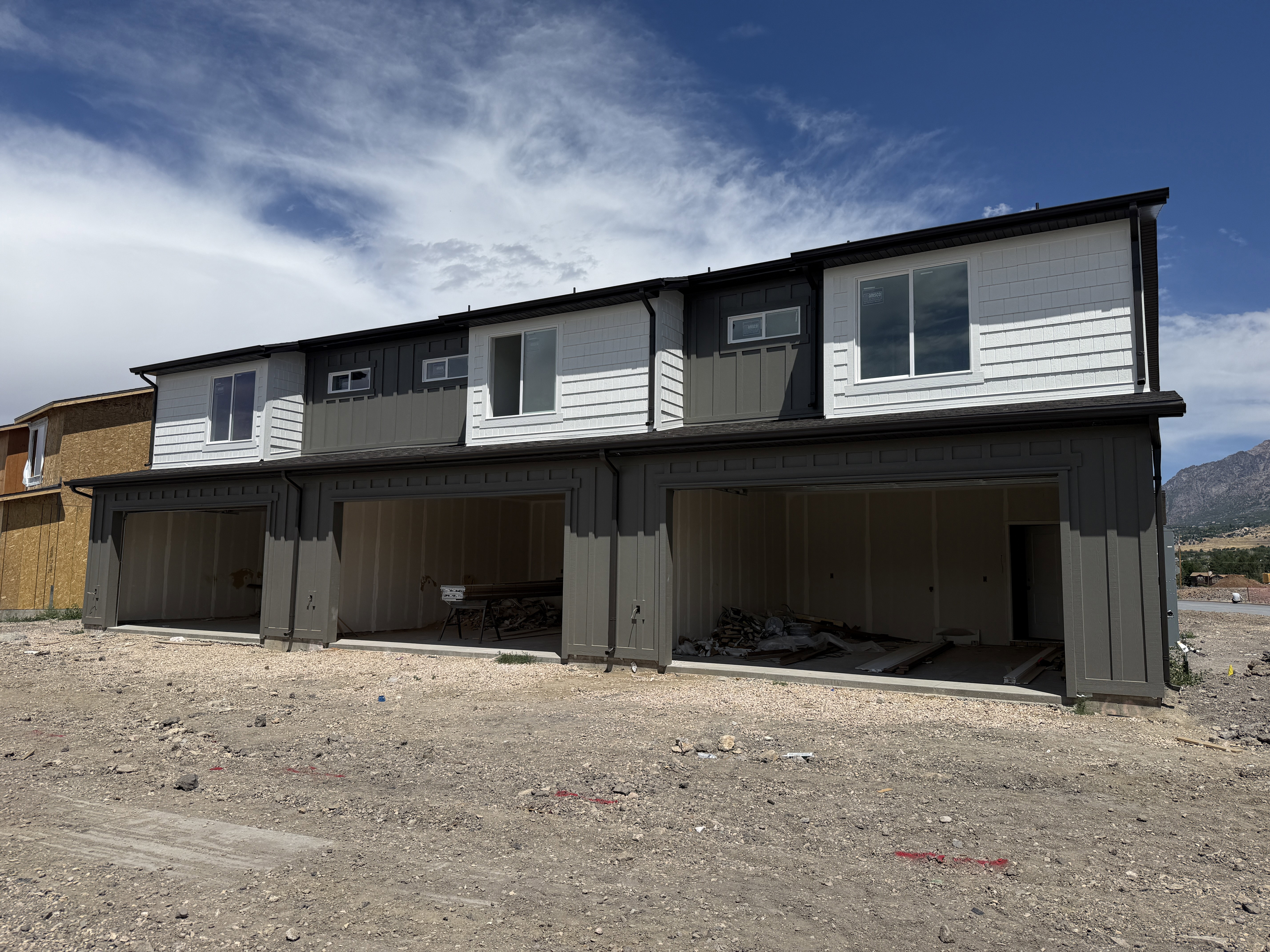 Contemporary townhome exterior featuring dual-tone siding, dark trim, multiple windows, and integrated garage bays